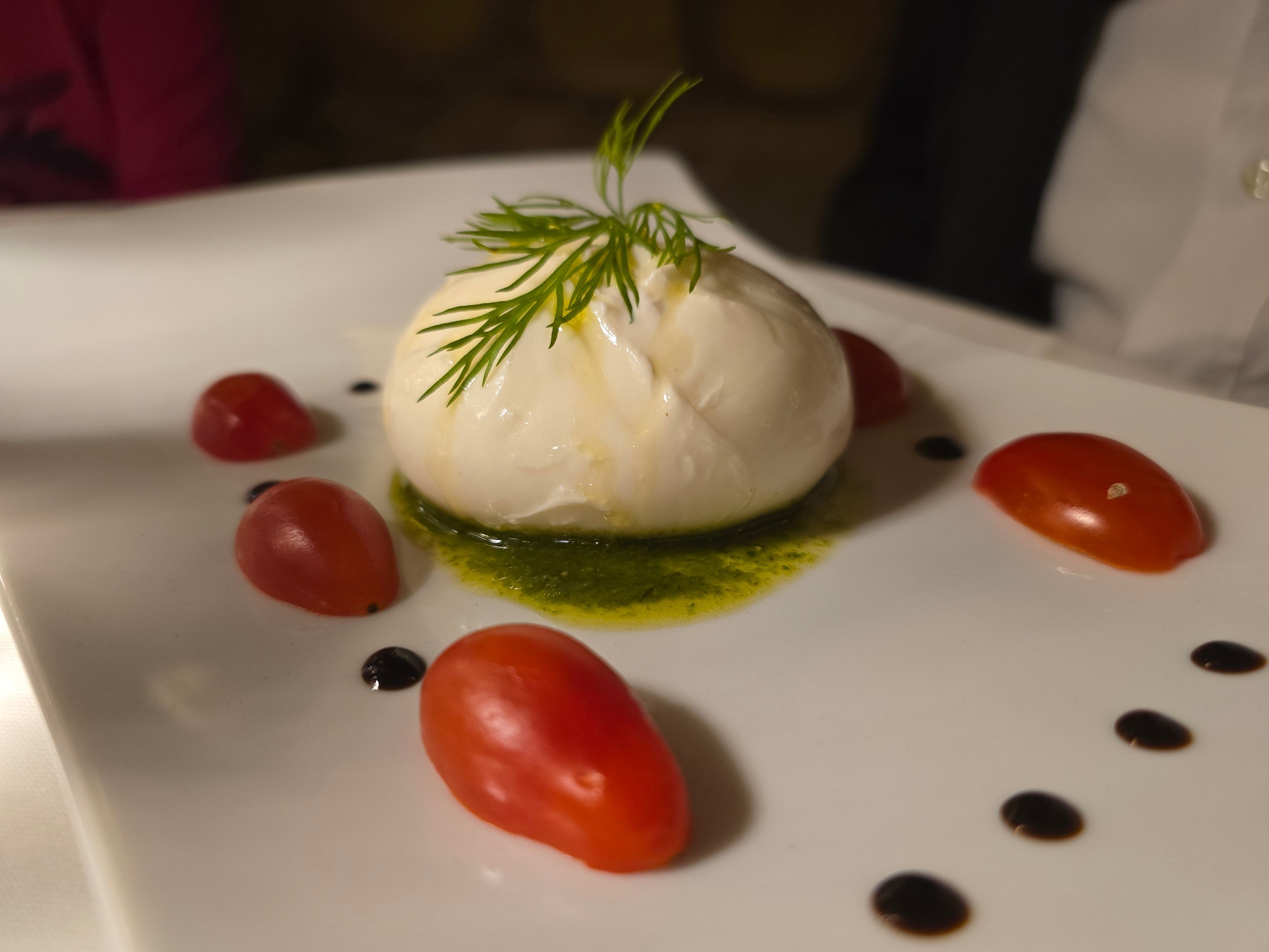 Eine Burrata-Kugel auf Pesto, drumrum sind Tomaten angerichtet.