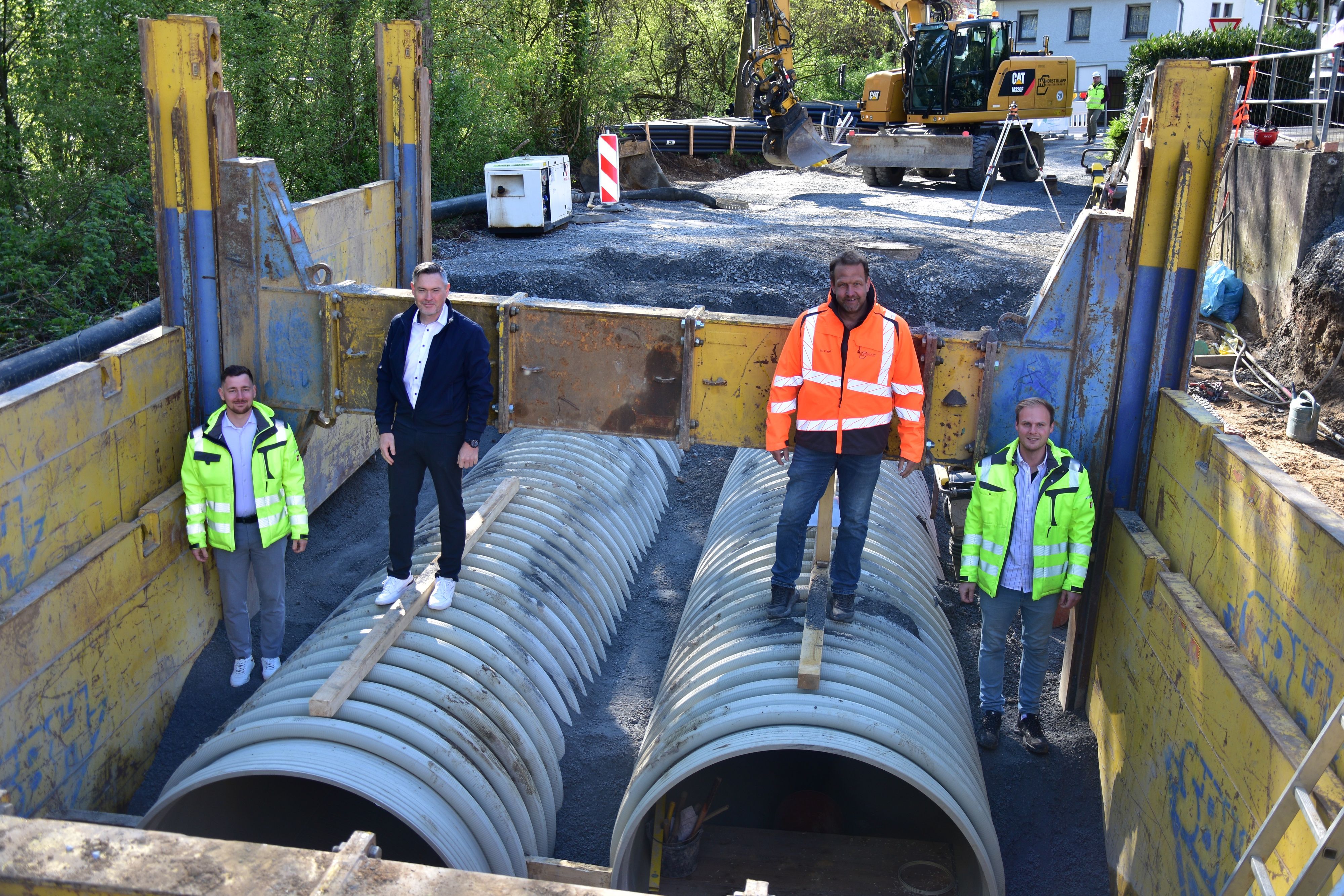 In der Baustelle für den neuen Stauraumkanal in Much stehen Michael Hoppe (Gemeindewerke Much), Bürgermeister Karsten Schäfer, Bauleiter Kai Vogel  und Kanalsanierungsberater Johannes Urbach auf den großen Röhren.