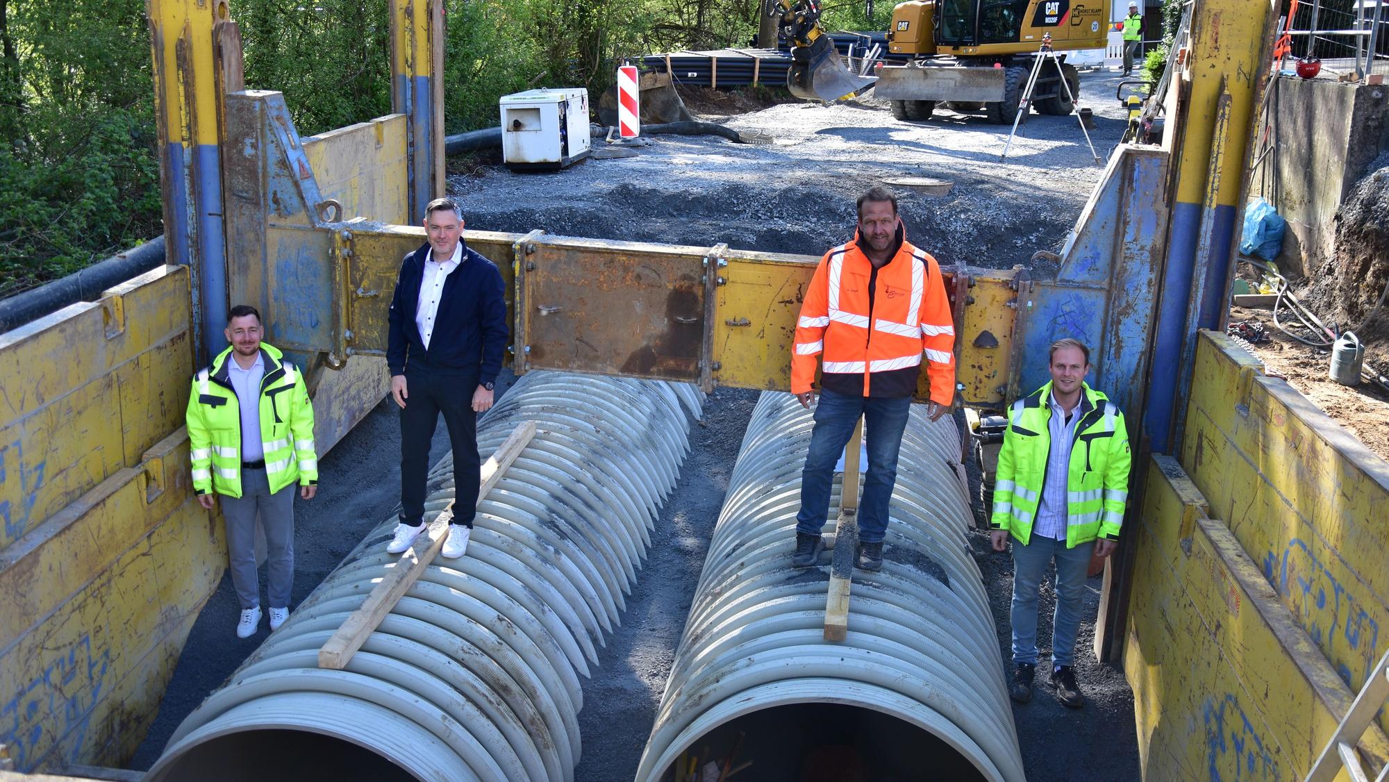 In der Baustelle für den neuen Stauraumkanal in Much stehen Michael Hoppe (Gemeindewerke Much), Bürgermeister Karsten Schäfer, Bauleiter Kai Vogel und Kanalsanierungsberater Johannes Urbach auf den großen Röhren.