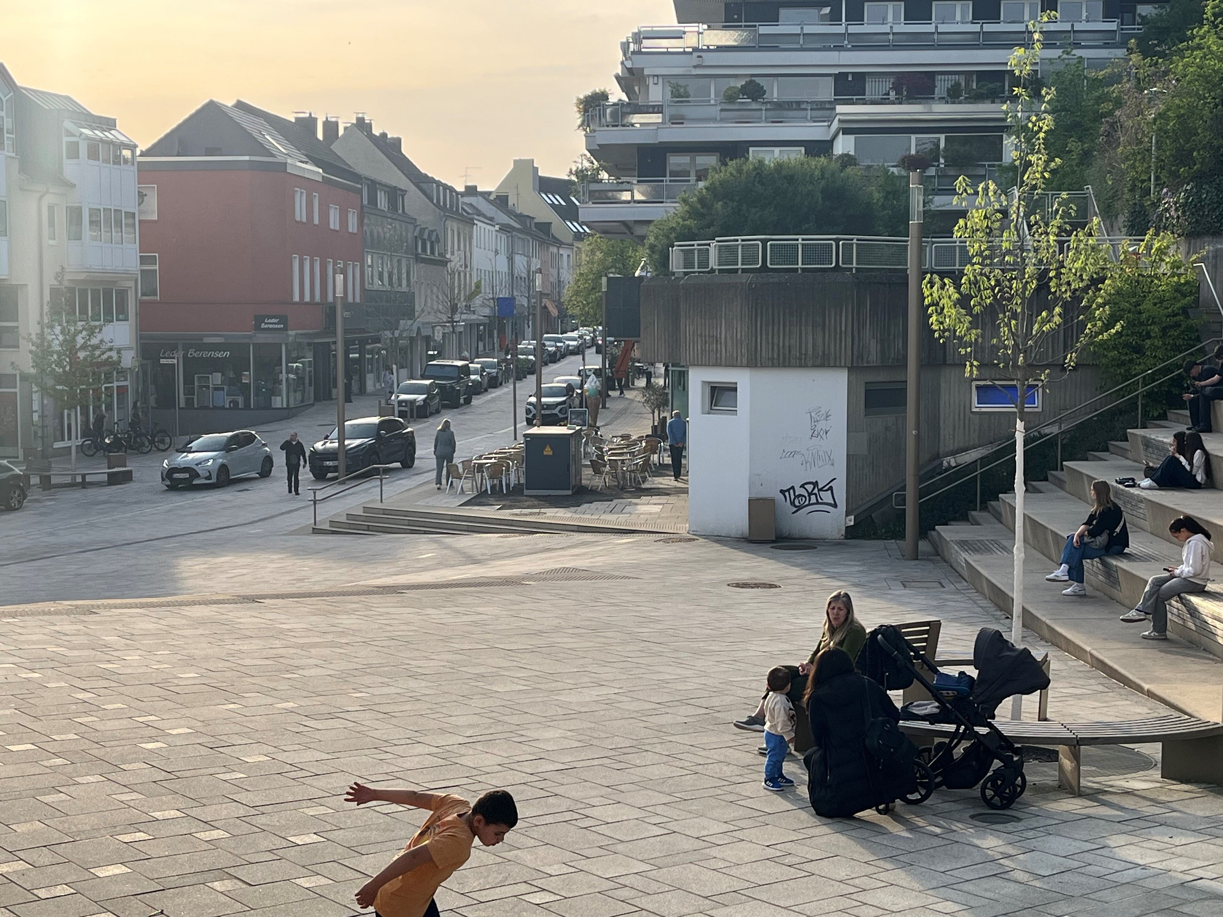 Menschen sitzen auf einer Bank, ein Junge spielt Fußball.