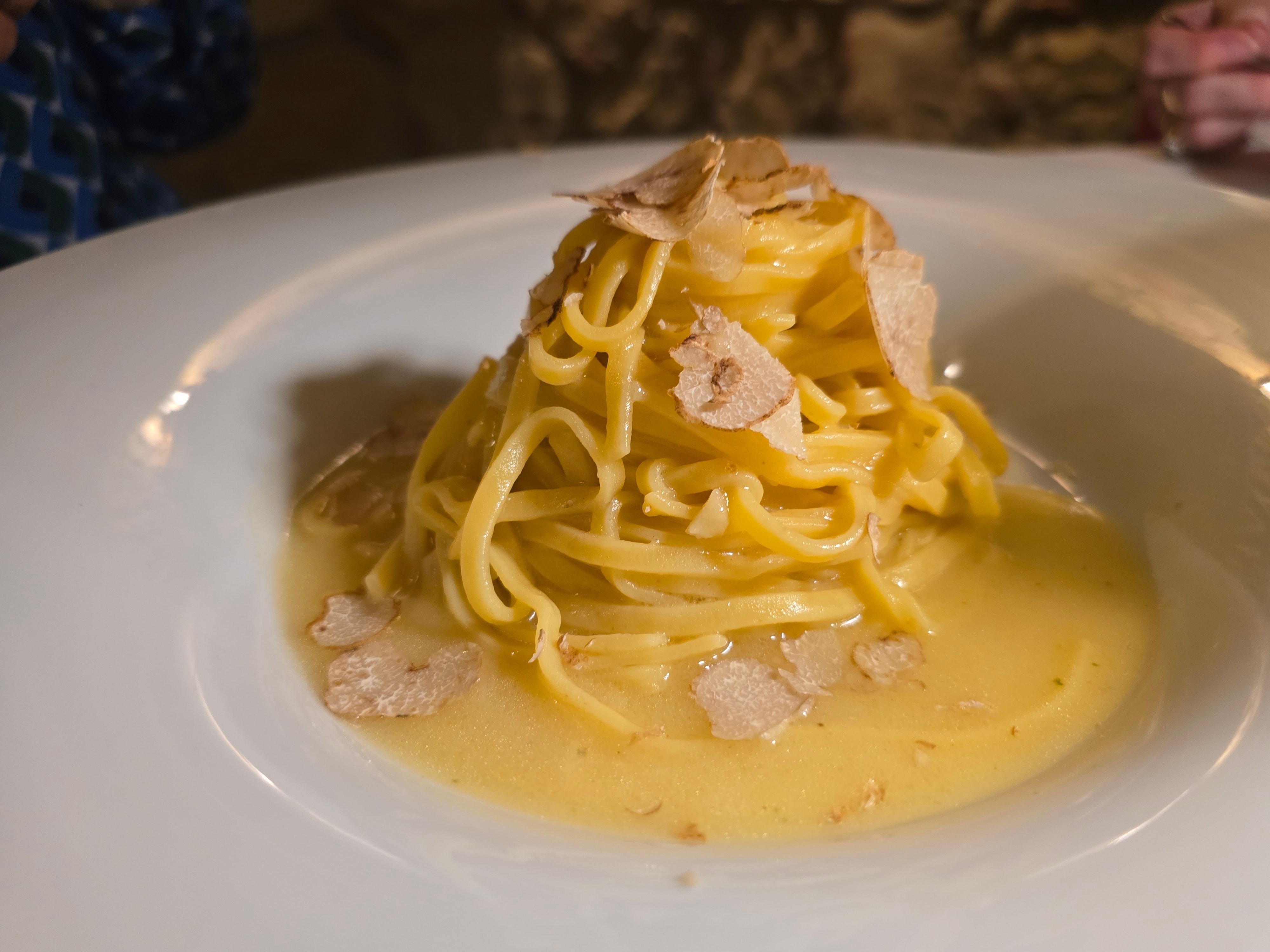 Die Nudeln liegen auf buttriger Sauce gehäuft und mit Trüffelhobeln garniert auf einem weißen Teller.