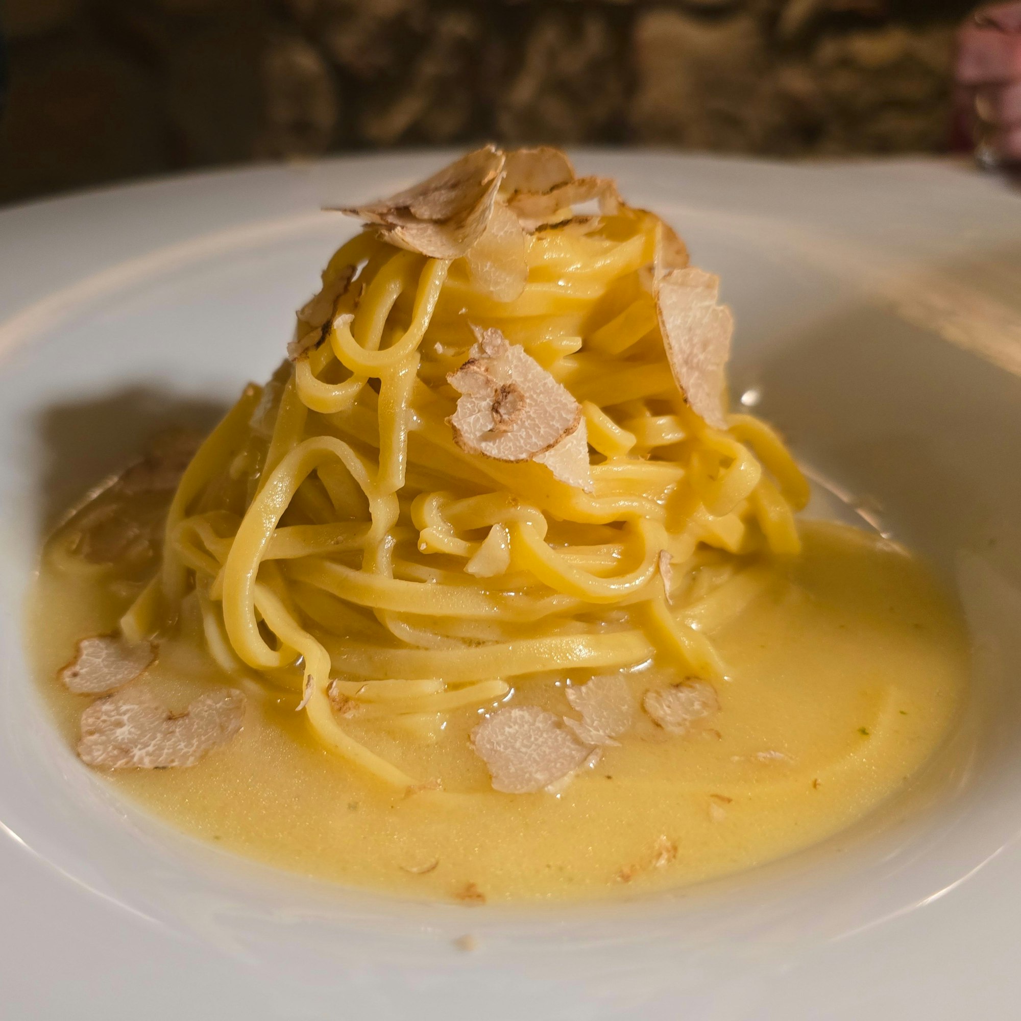 Die Nudeln liegen auf buttriger Sauce gehäuft und mit Trüffelhobeln garniert auf einem weißen Teller.