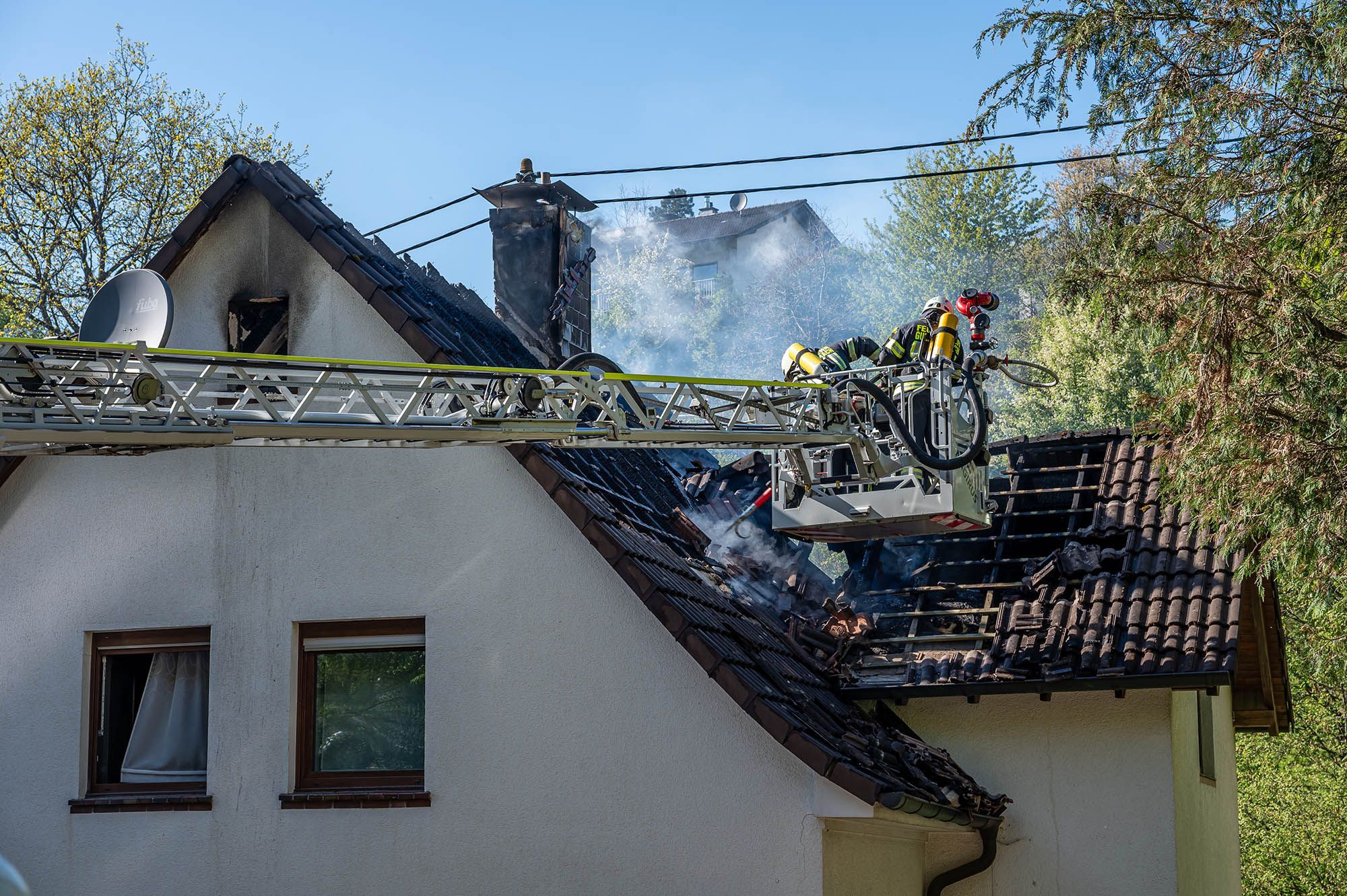 Feuerwehrleute löschen von einer Drehleiter aus einen Dachstuhlbrand.