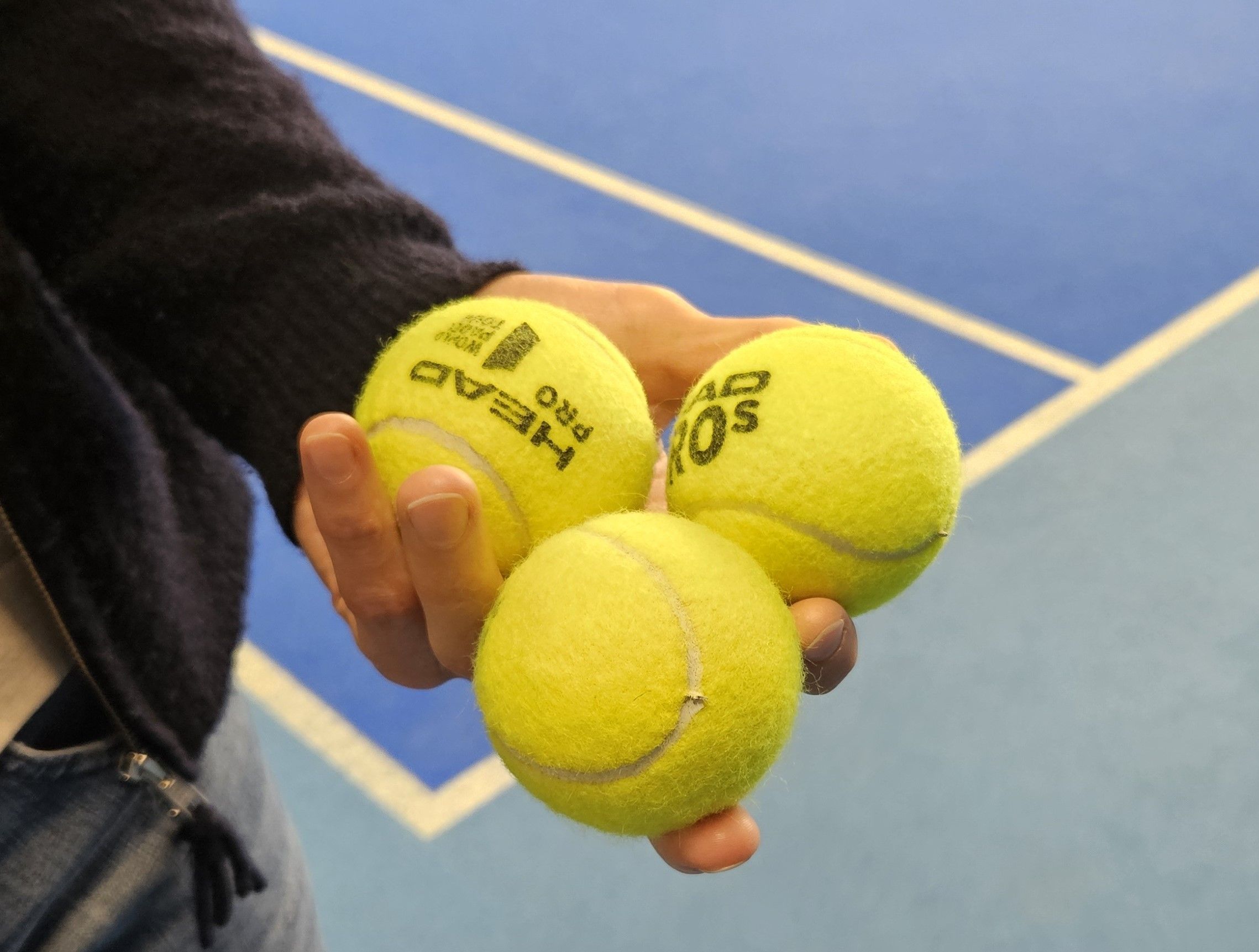 Jemand hält drei Padel-Bälle in der Hand.