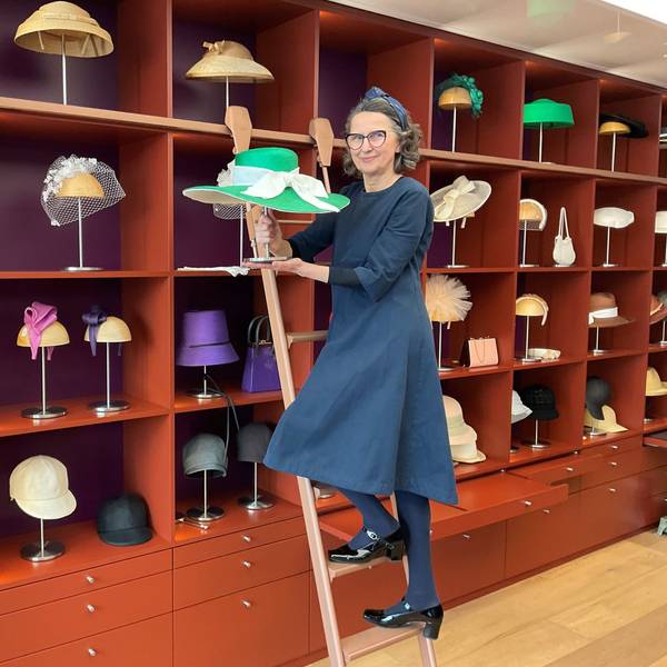 Eine Frau steht auf einer Leiter, die vor einem großen Regal mit Hüten steht.