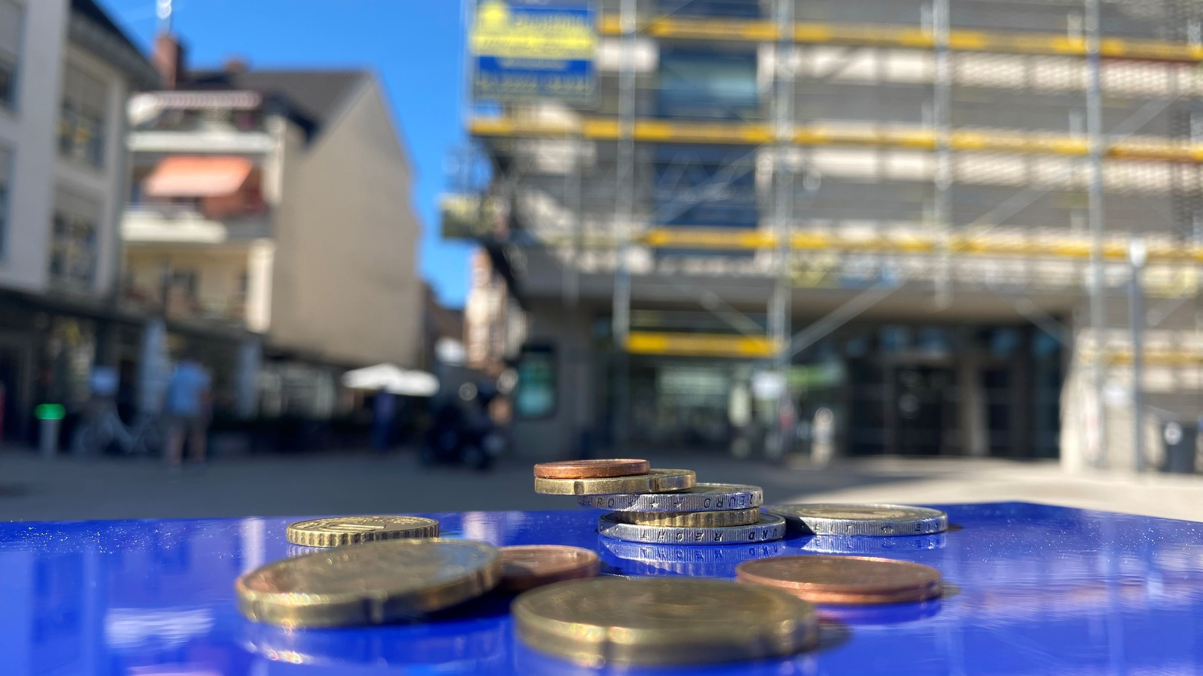 Zu sehen sind Münzen und im Hintergrund das Brühler Rathaus.