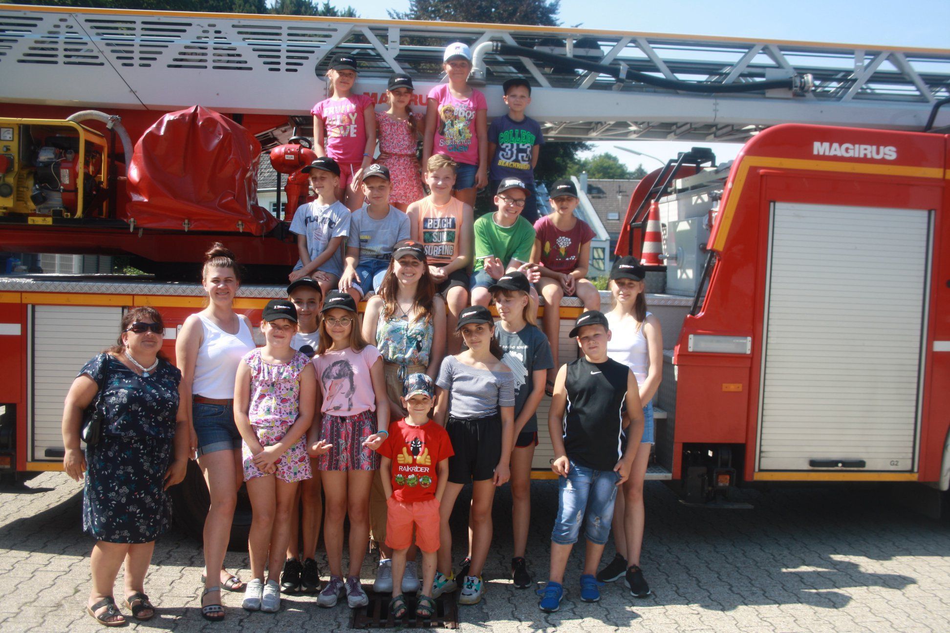 Eine Gruppe von Kindern und Betreuerinnen steht um und auf einem Drehleiterfahrzeug der Feuerwehr.