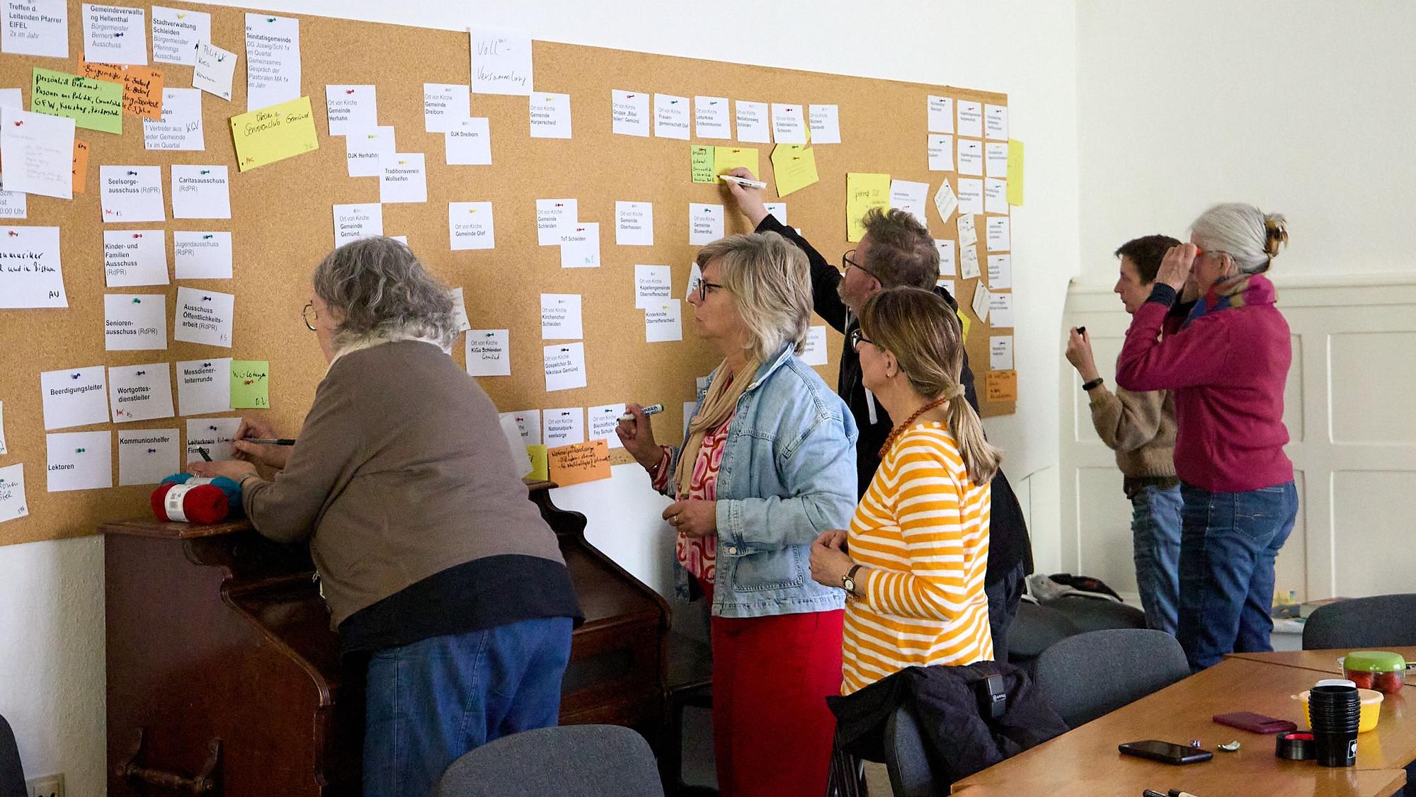 Das Pastoral- und Leitungsteam heftet Zettel an eine Pinnwand und beschreibt das Papier.
