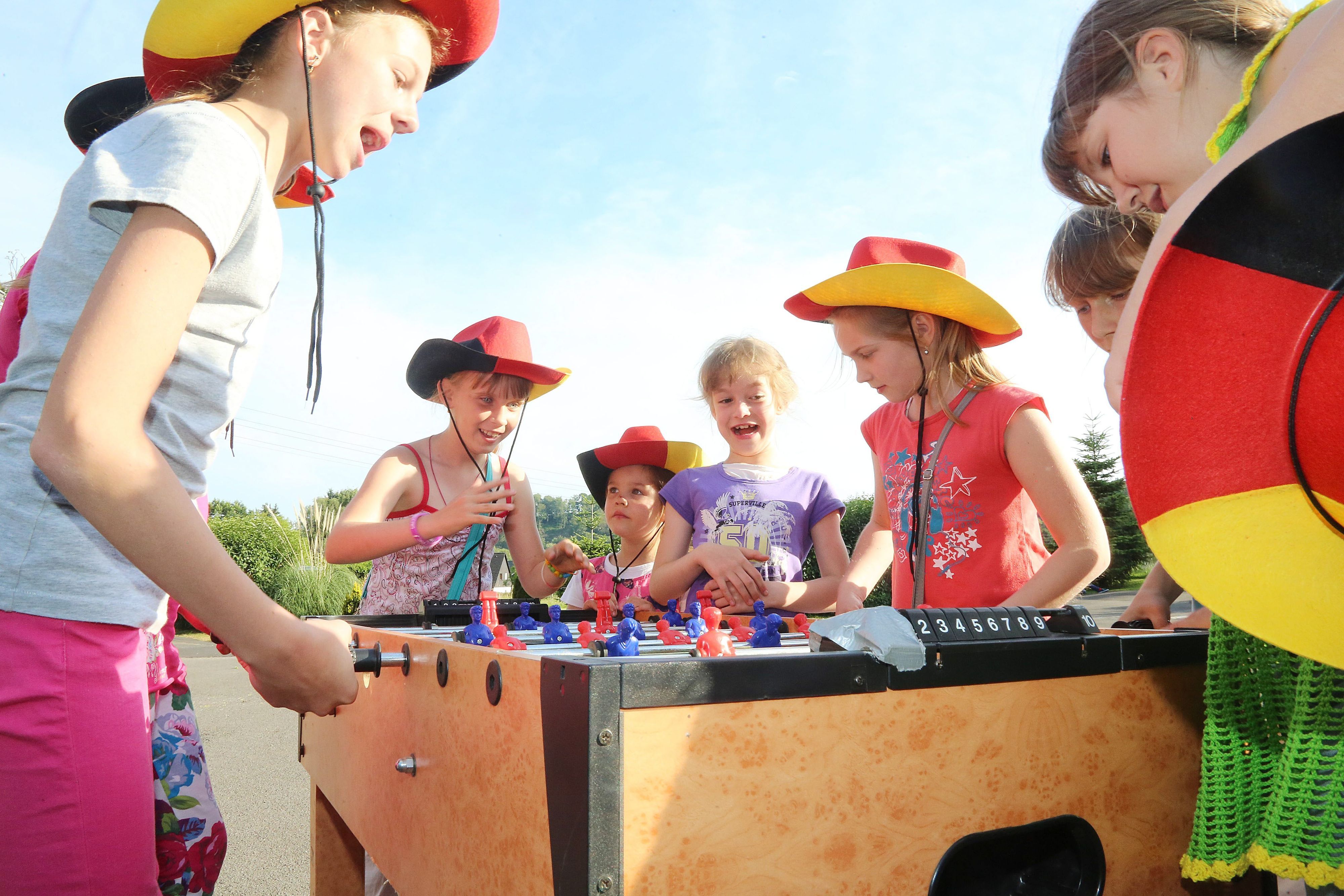 Kinder mit Hüten in Schwarz-Rot-Gold spielen an einem Tischkicker.