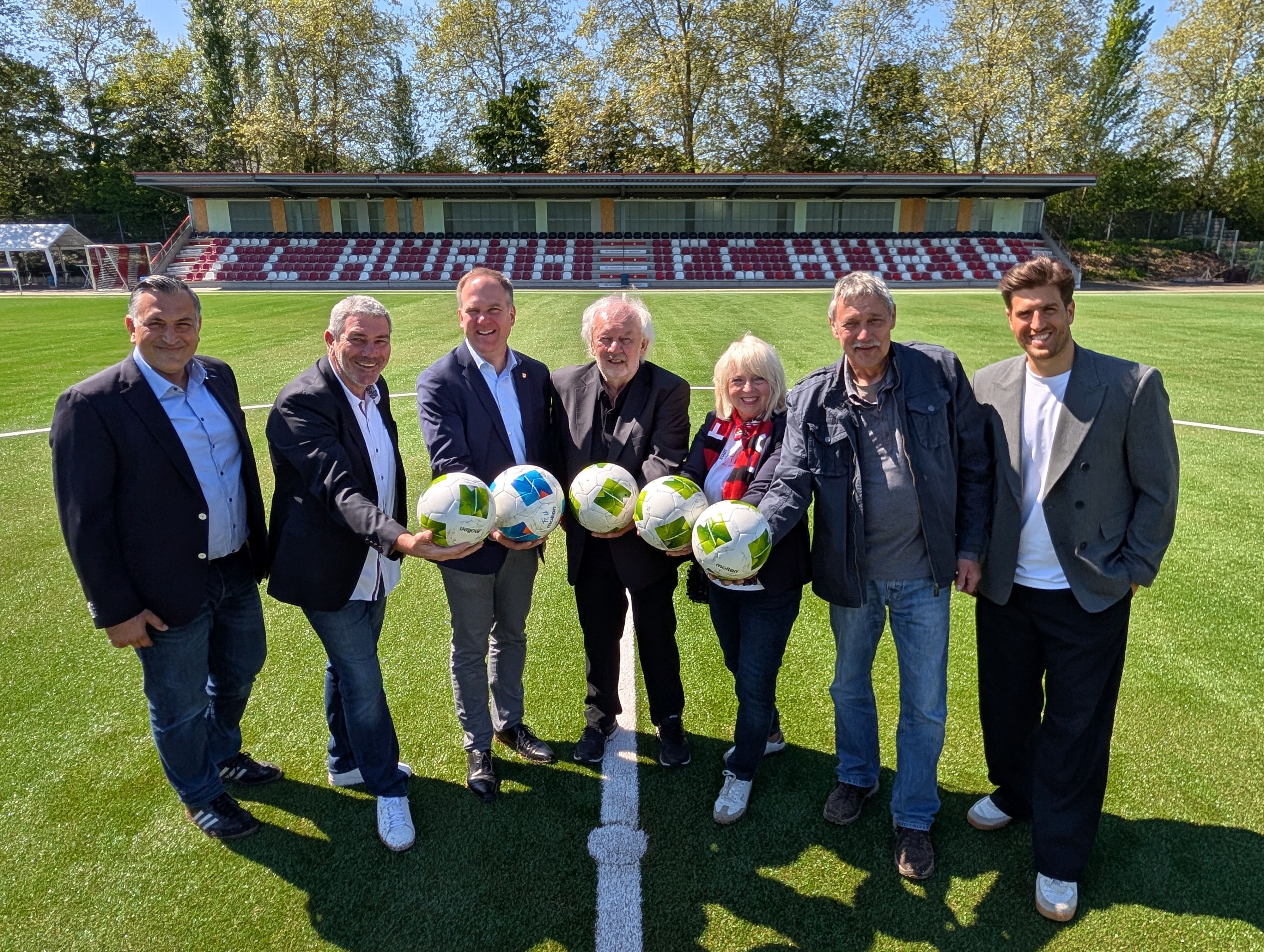 Das Foto zeigt Vertreterinnen und Vertreter der Stadt und des FC Hürth auf dem Kunstrasen vor der Tribüne im Salus-Park.