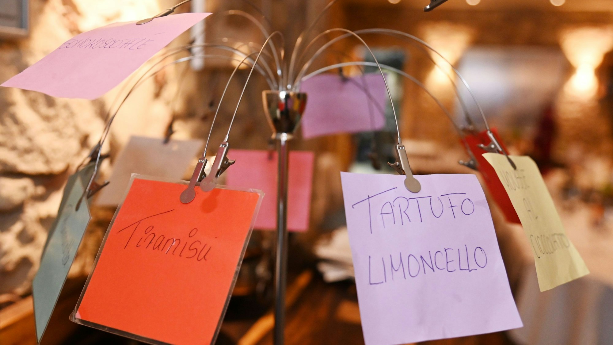 Eine Haltevorrichtung mit Clips, an der Zettel mit den Desserts auf buntem Papier hängen.