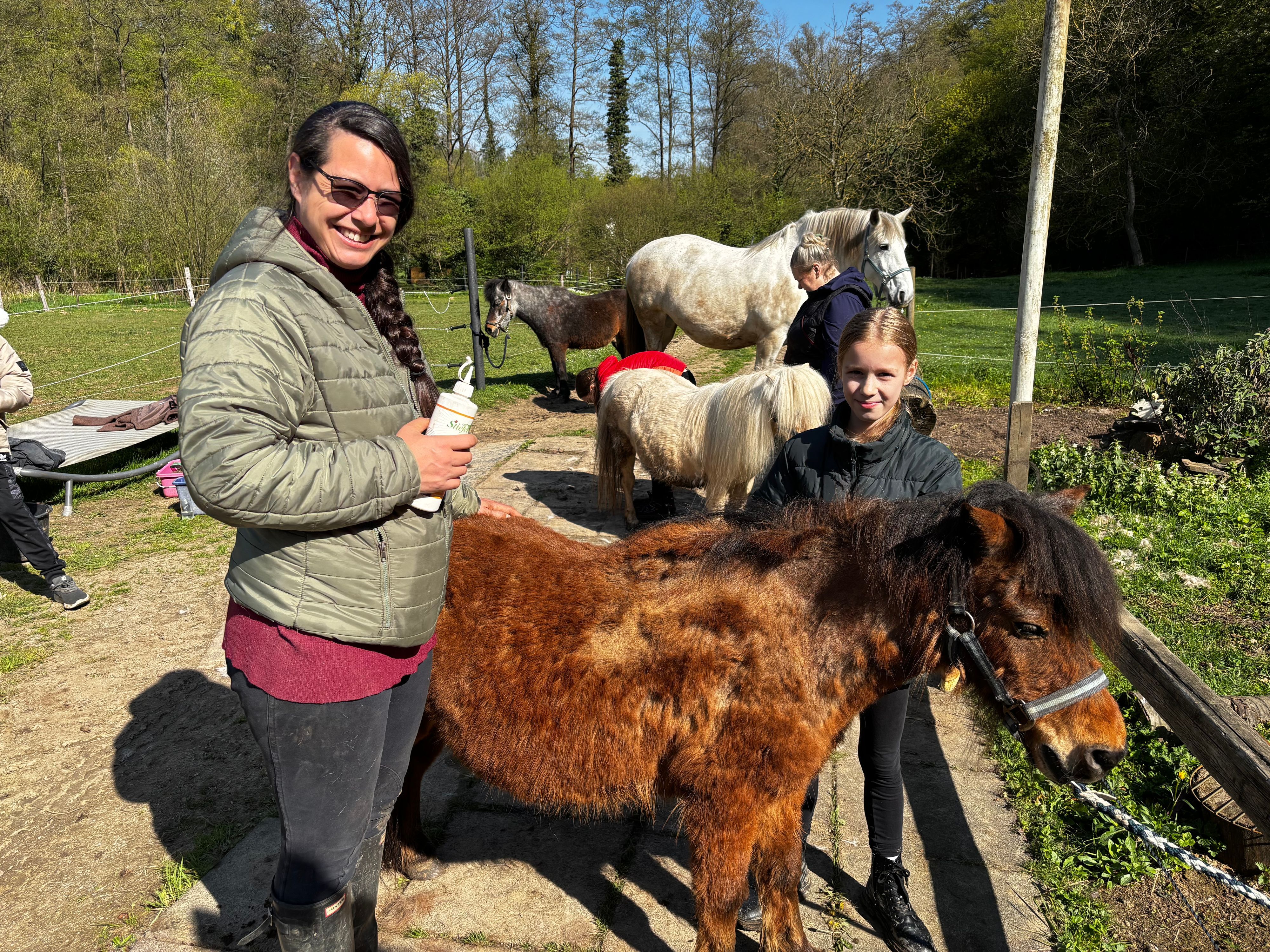 Eine Frau und ein Mädchen blicken lächelnd in die Kamera. Ein braunes Shetlandpony steht zwischen ihnen.