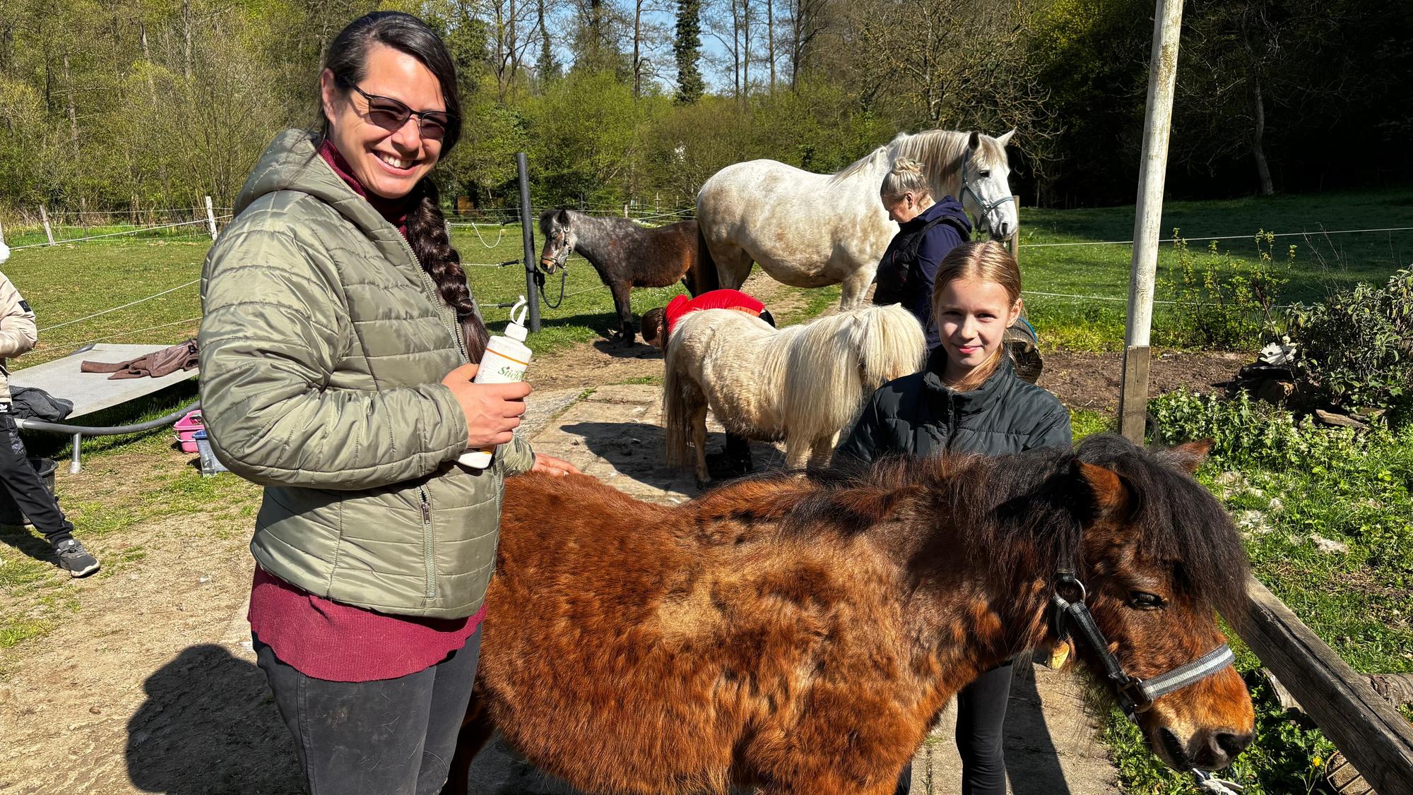 Eine Frau und ein Mädchen blicken lächelnd in die Kamera. Ein braunes Shetlandpony steht zwischen ihnen.