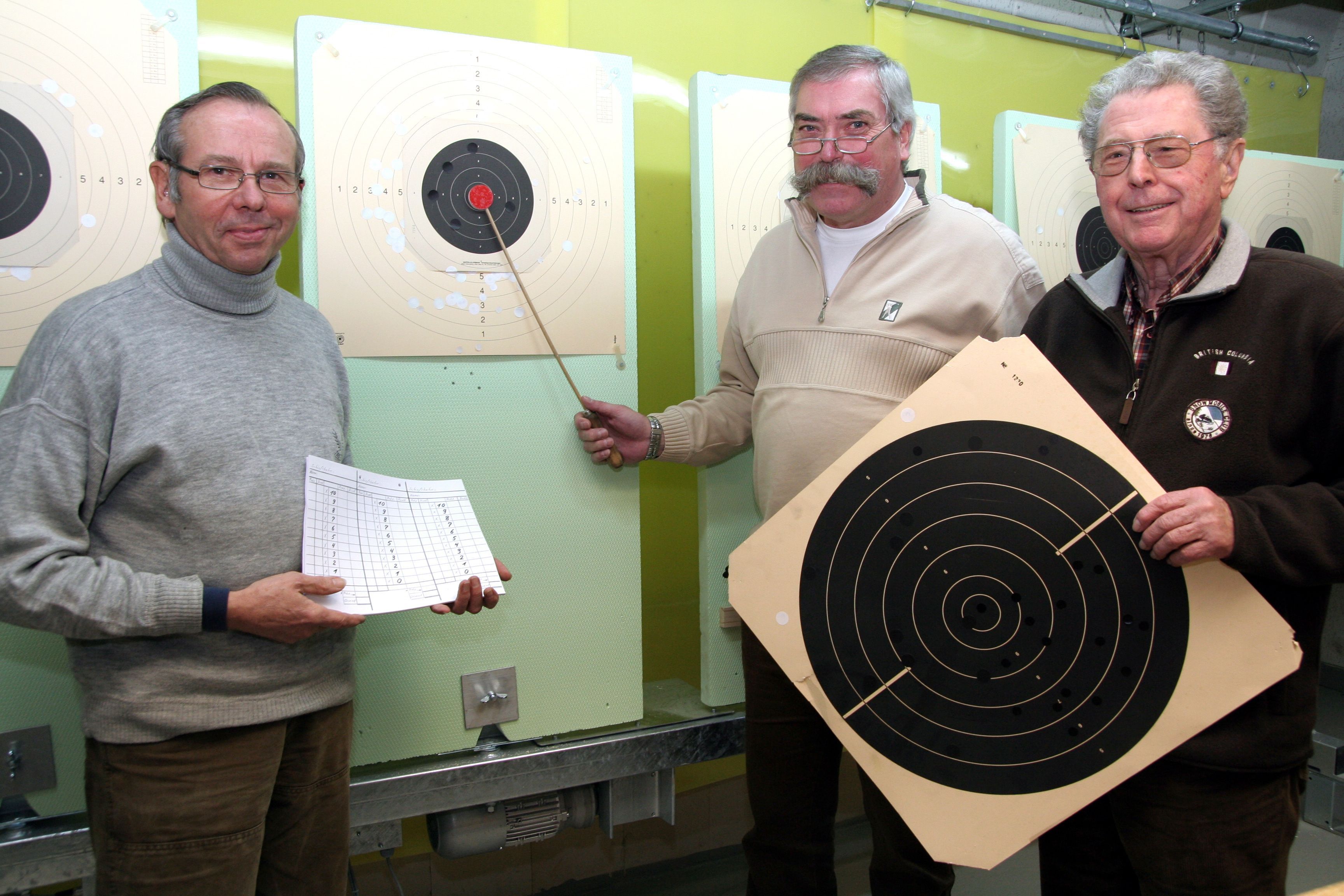 Drei Sportschützen stehen an einer Zielscheibe.
