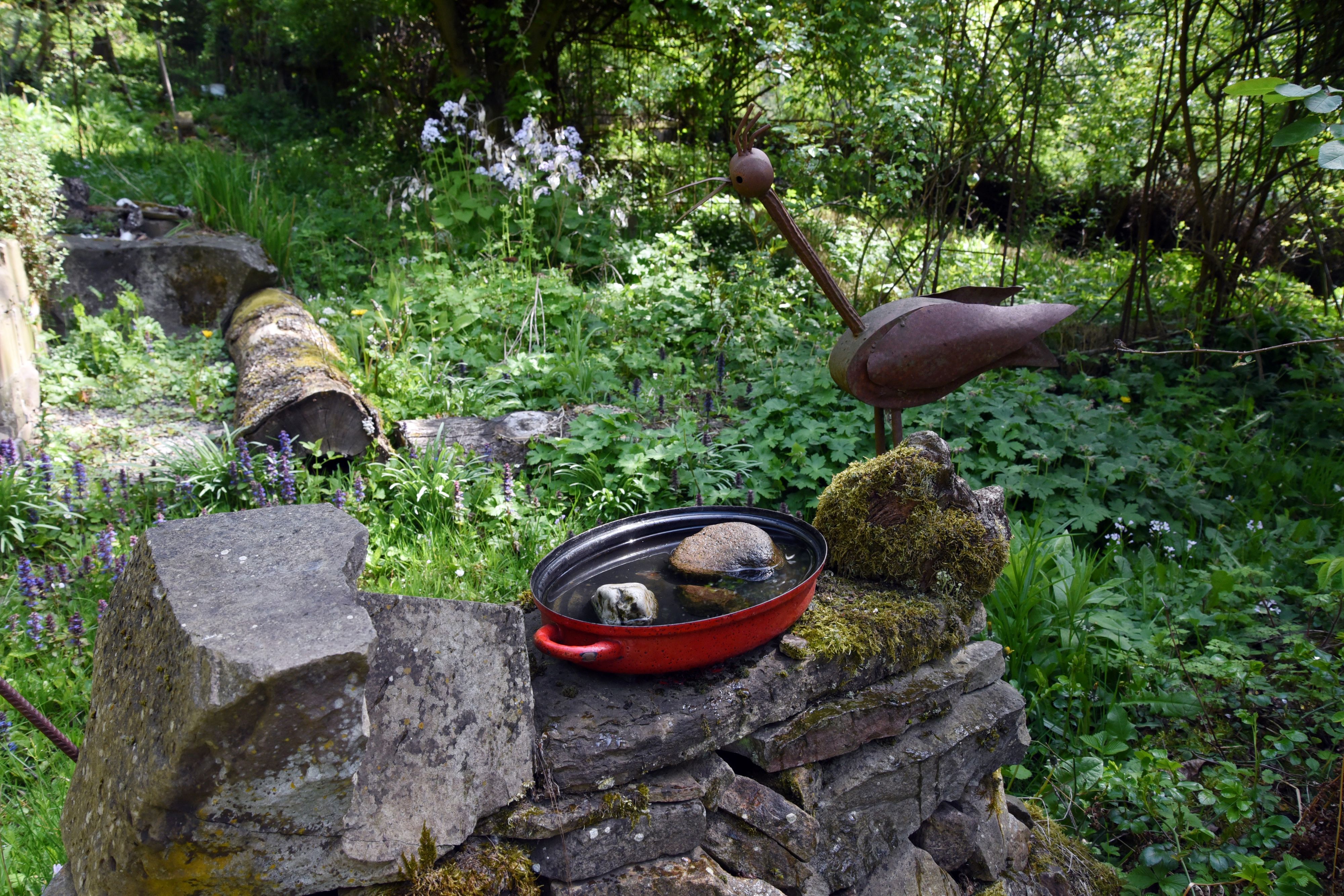Ein Metallvogel auf einer Gartenmauer.