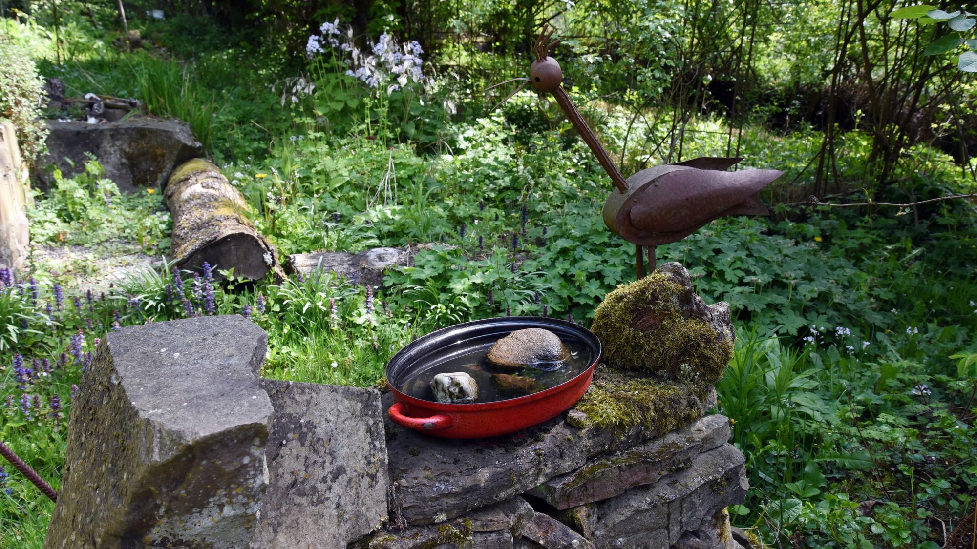 Ein Metallvogel auf einer Gartenmauer.