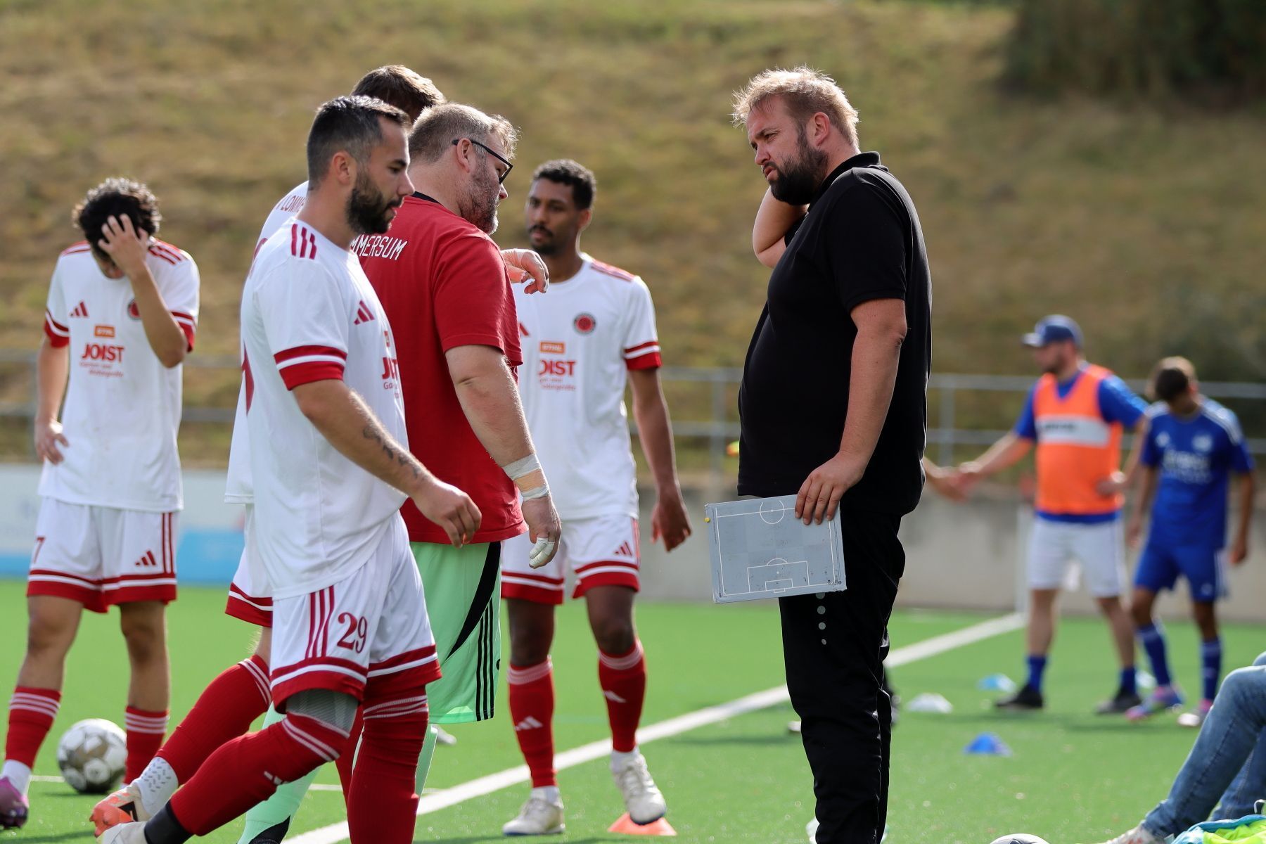 Sebastian Reisenauer steht am Spielfeldrand, In der Hand hält er eine kleine Taktiktafel.