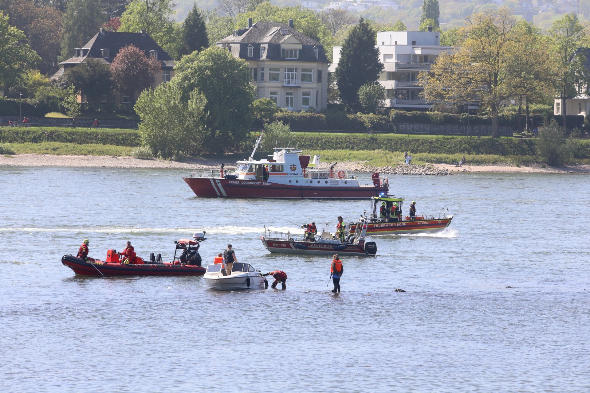 Mehrere Schiffe, darunter Feuerwehrboote auf dem Rhein neben einem kleinen Sportboot.