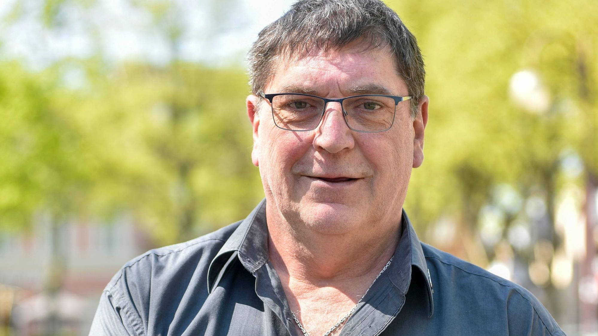 Das Foto zeigt das Portrait eines Mannes mit Brille und einem grauen Hemd.