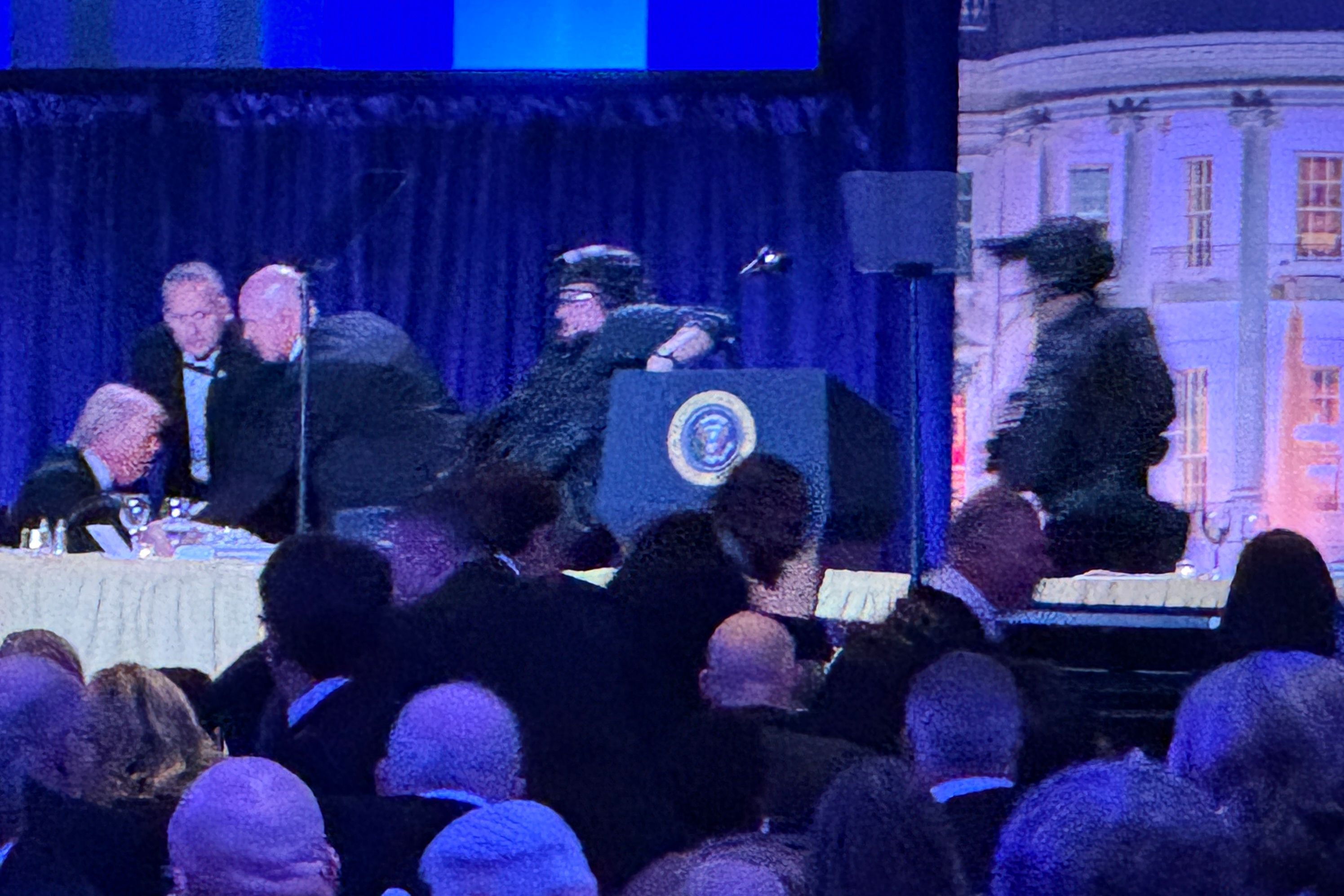 US-Präsident Donald Trump (l) sitzt auf der Bühne, während Agenten des US-Geheimdienstes ihn nach einem Vorfall außerhalb des Ballsaals während des White House Correspondents' Dinner aus dem Ballsaal bringen.