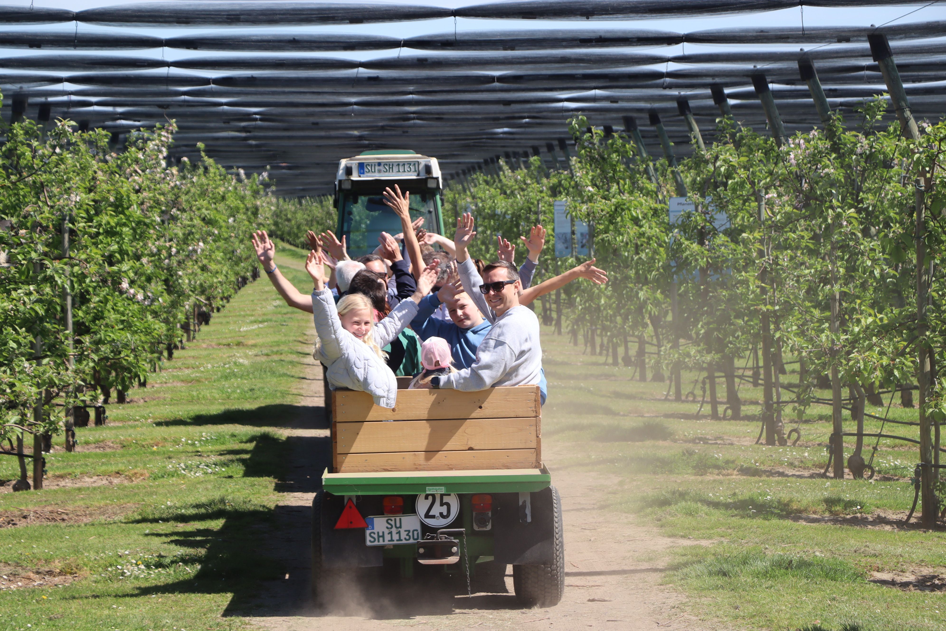 Menschen winken vom Anhänger bei Traktorfahrten durch die Plantagen