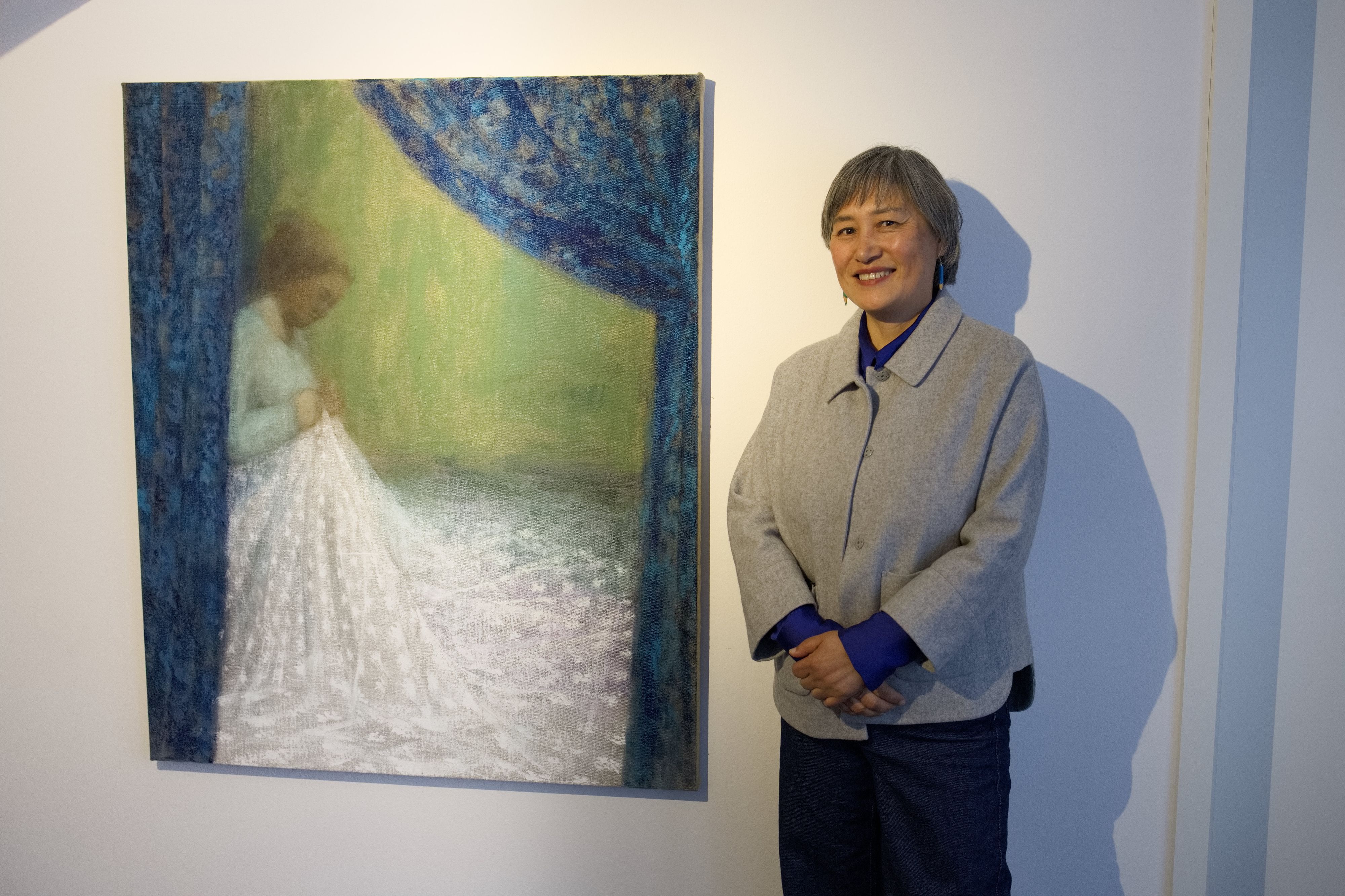 Die Künstlerin vor ihrem Bild, auf dem eine Frau an einem weißen Kleid näht.