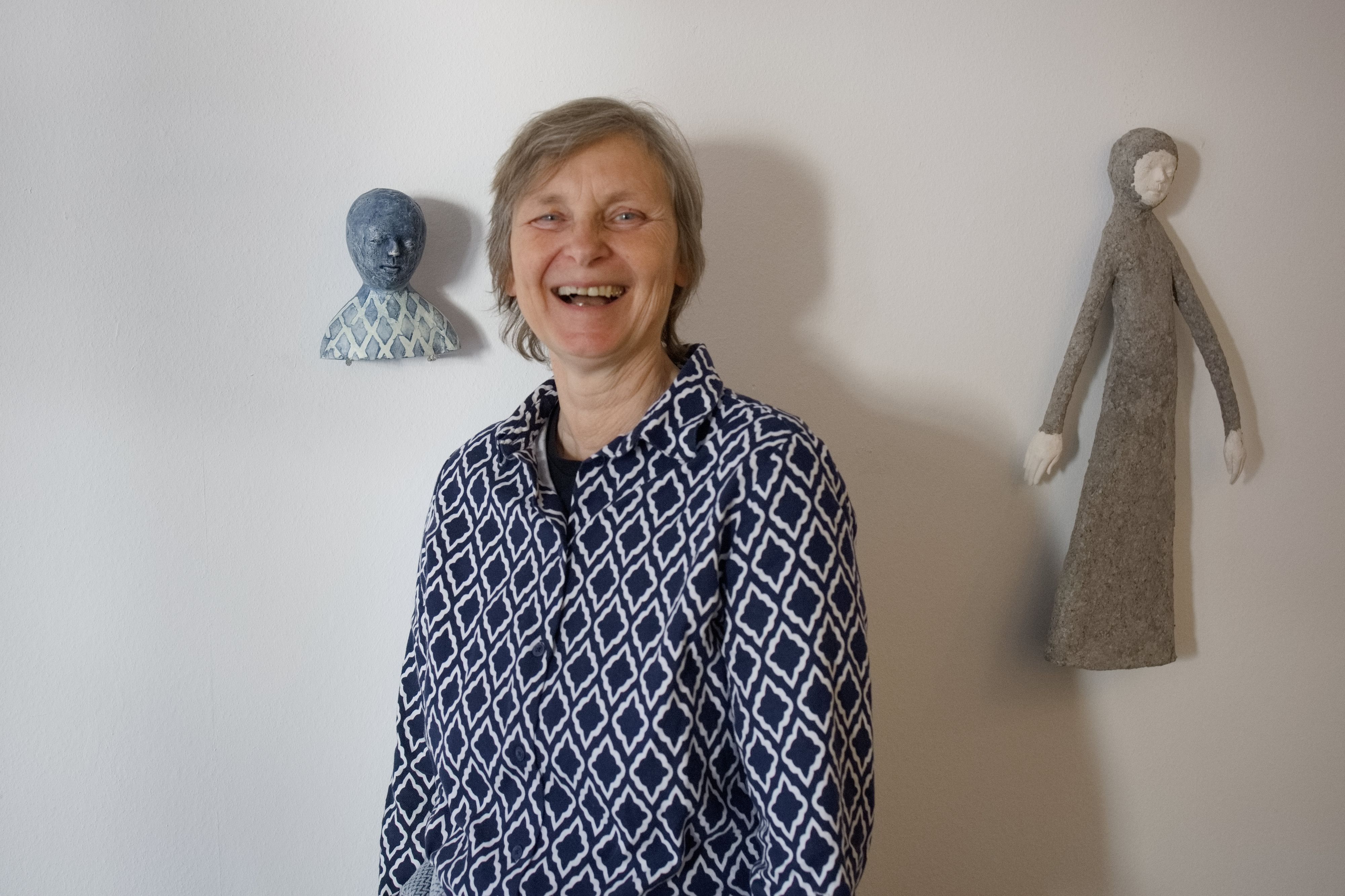 Die Künstlerin vor der Tonskulptur. Beide tragen blau-weiß karierte Blusen.