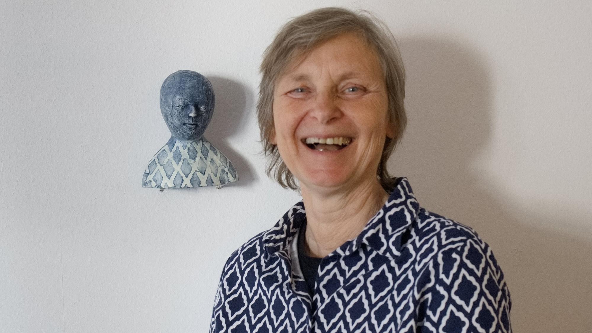 Die Künstlerin vor der Tonskulptur. Beide tragen blau-weiß karierte Blusen.