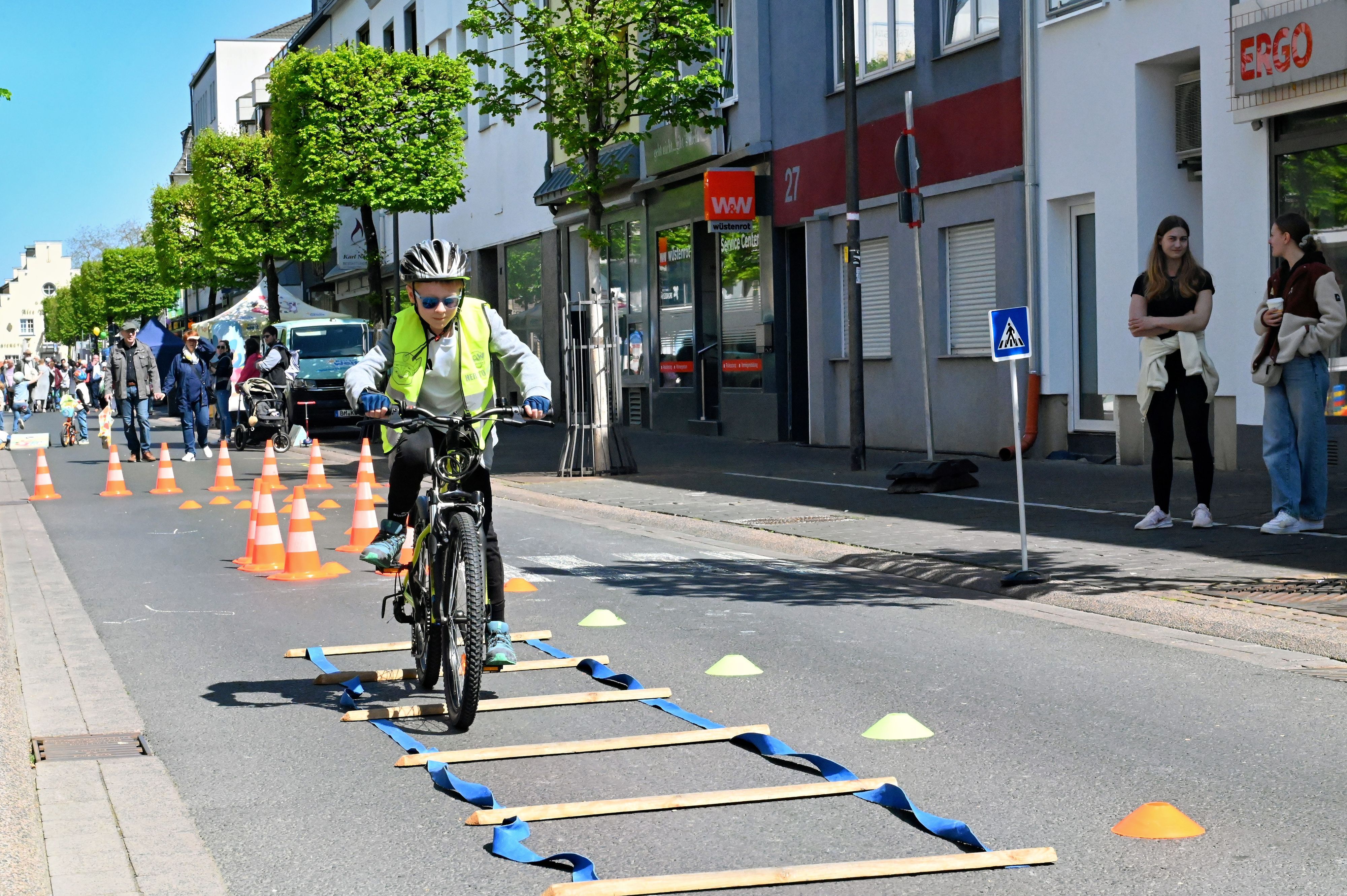 Mit Helm und Warnweste durchfährt der Siebenjährige mit seinem Rad den Hindernisparcours mit Pylonen und Holzschwellen auf der Straße.
