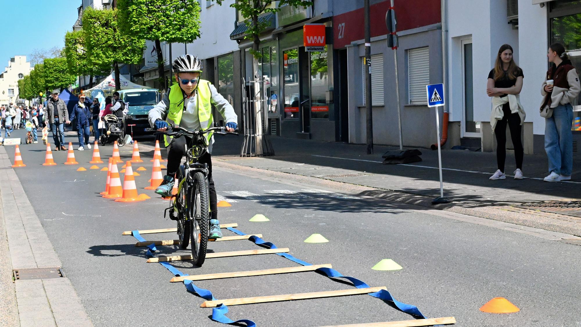 Mit Helm und Warnweste durchfährt der Siebenjährige mit seinem Rad den Hindernisparcours mit Pylonen und Holzschwellen auf der Straße.