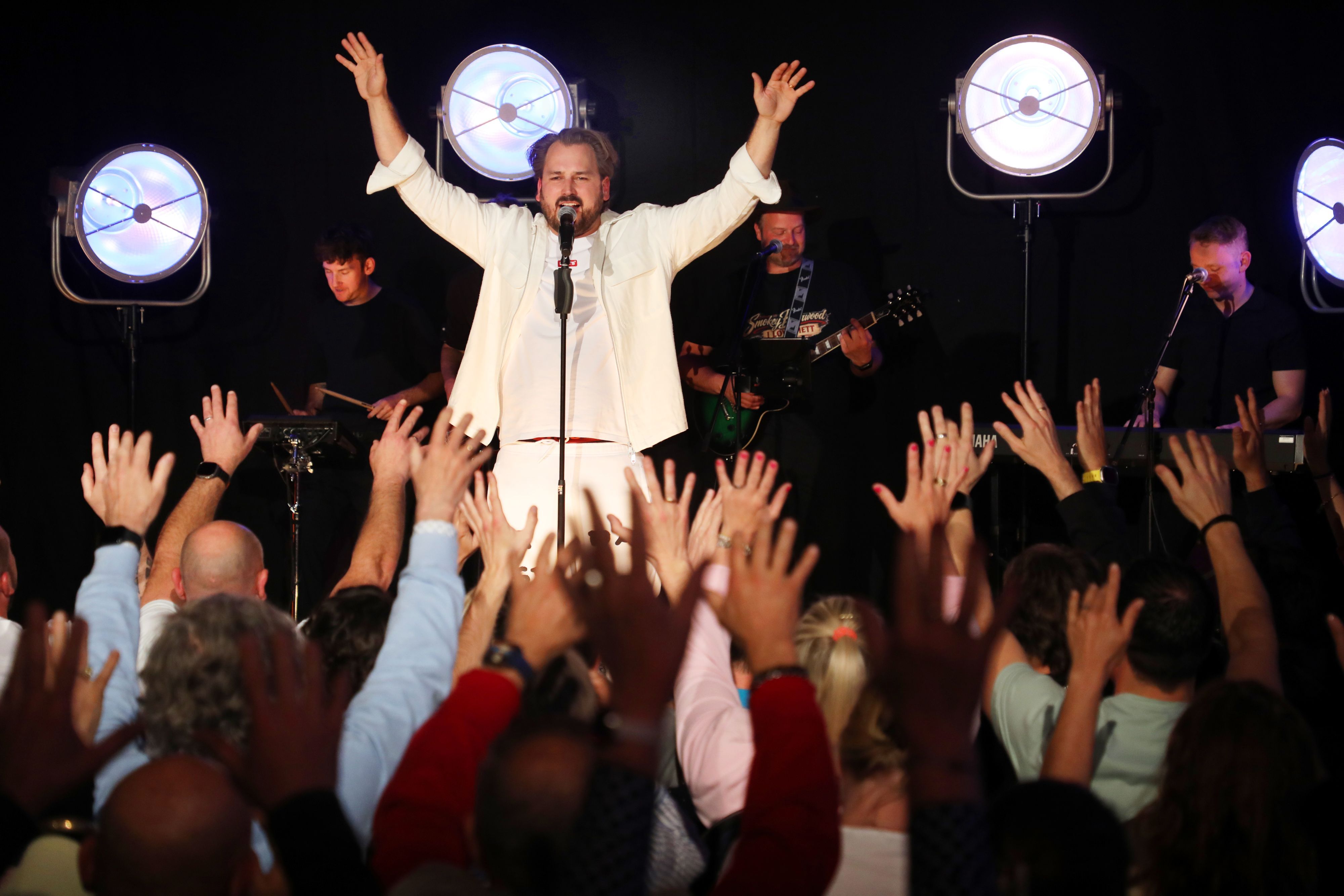Ein Mann auf einer Bühne reckt die Hände in die Höhe so wie das Publikum vor ihm.