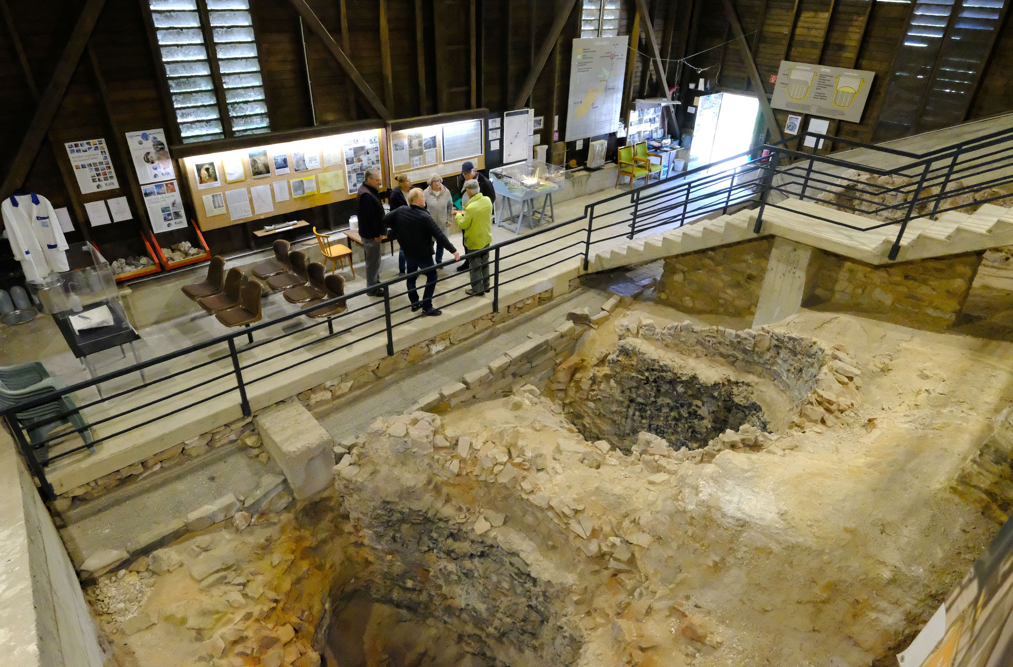Besucher in der römischen Kalkbrennerei in Iversheim nehmenan einer Führung teil. Im Vordergrund sind die Überreste von zwei römischen Kalköfen zu sehen.