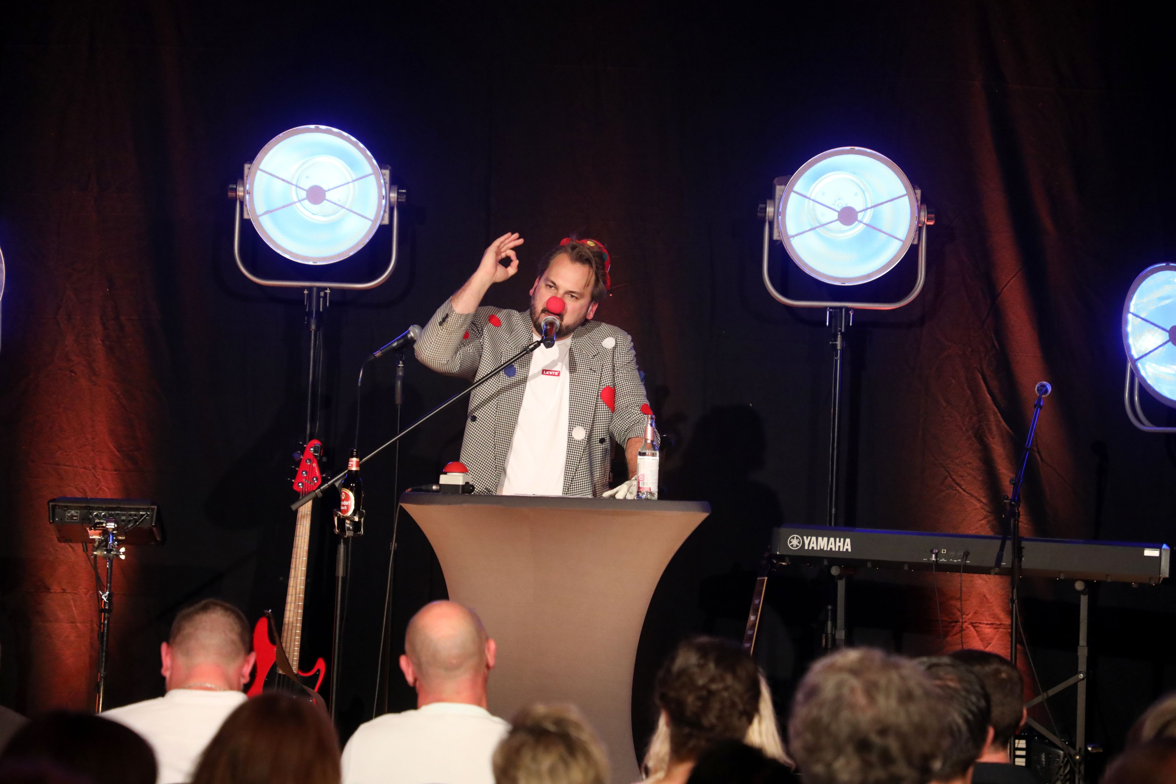 Ein Mann steht als Büttenredner mit Pappnase auf einer Bühne.