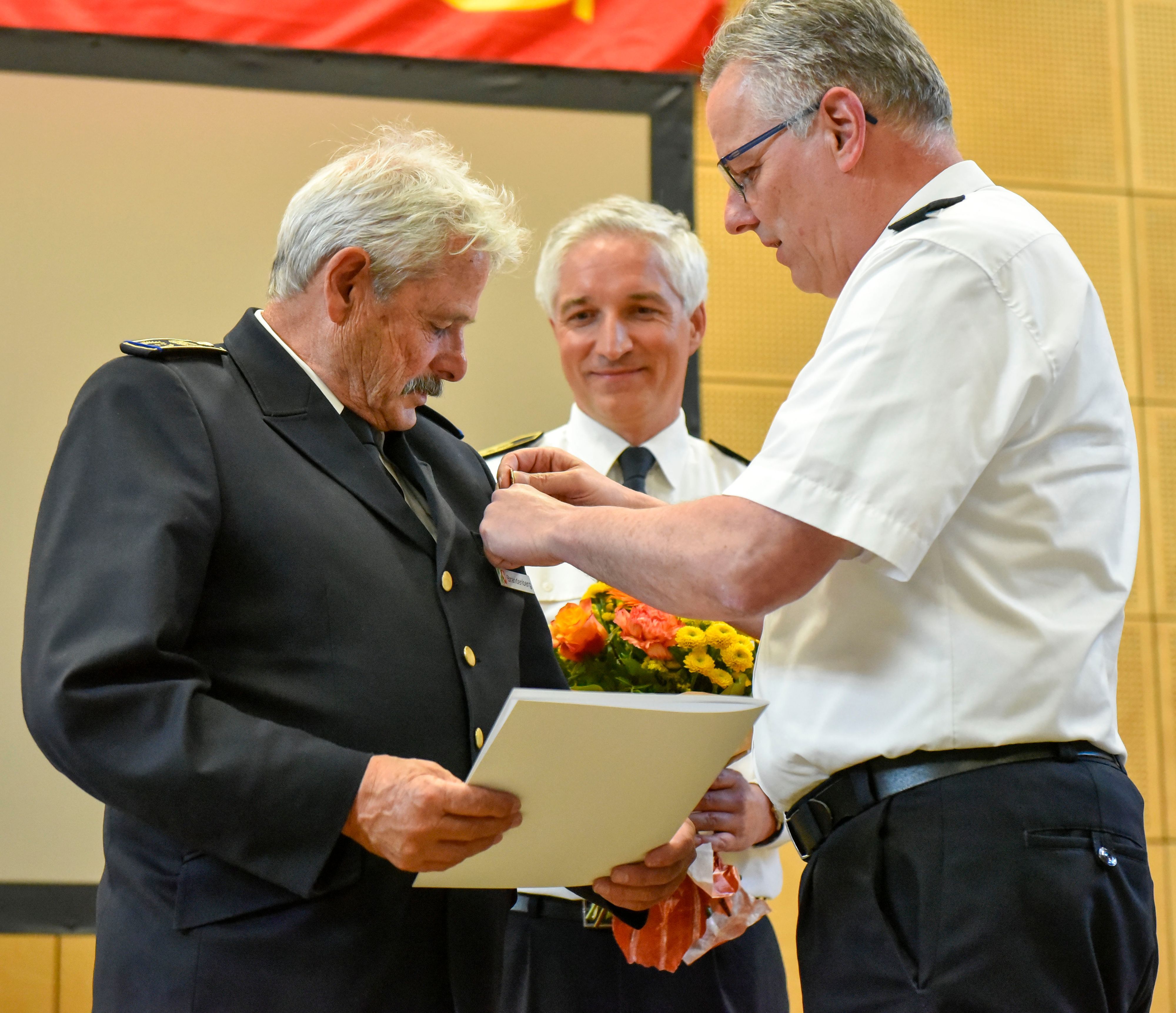 Auf dem Bild ist ein Feuewehrmann zu sehen, der geehrt wird.