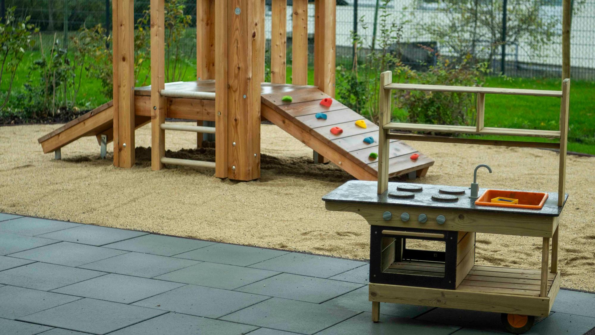 Eine Spielküche und ein Klettergerüst im Außenbereich einer Kita.