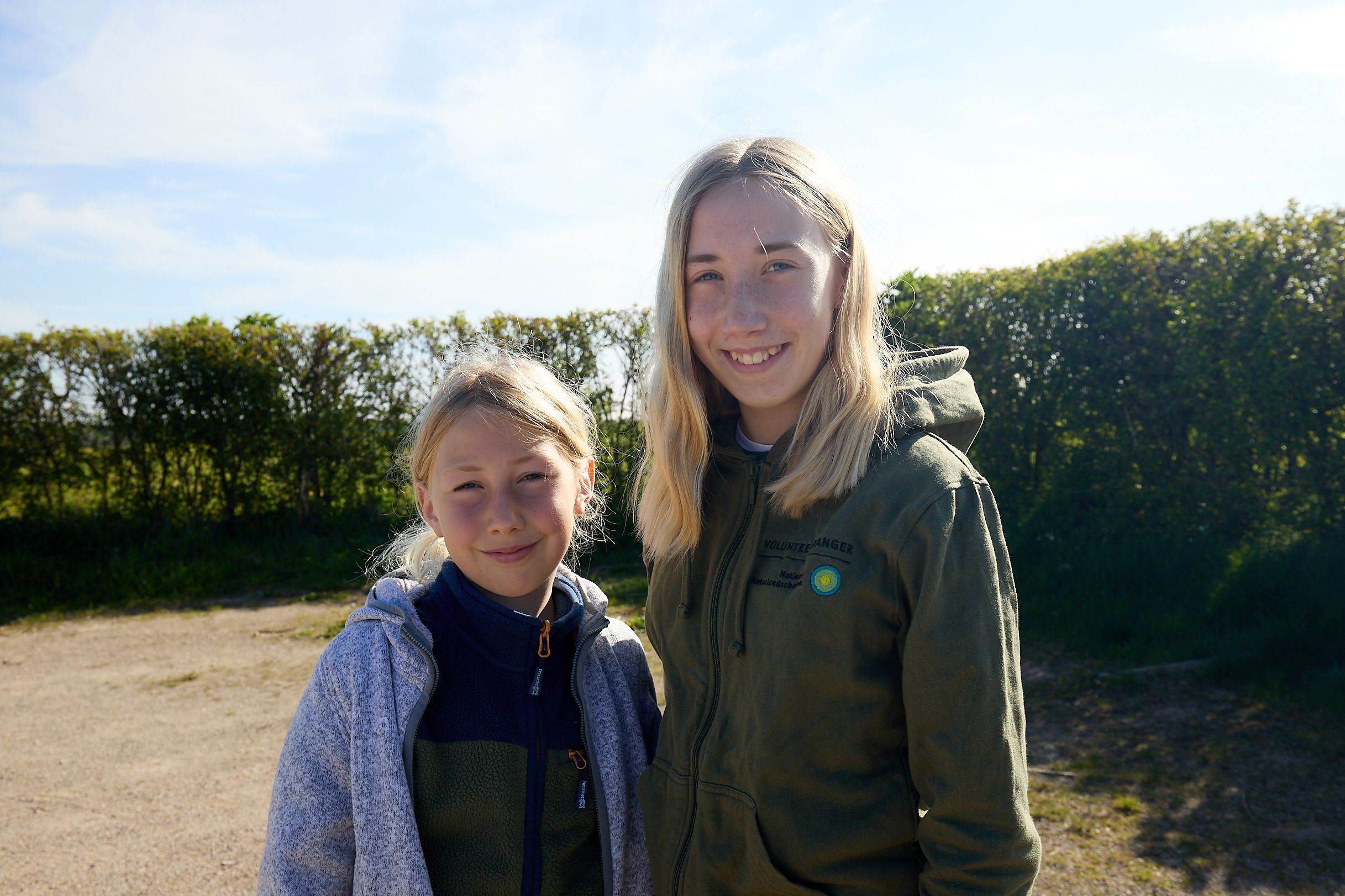 Beide Geschwister haben blonde Haare und schauen lächelnd in die Kamera.