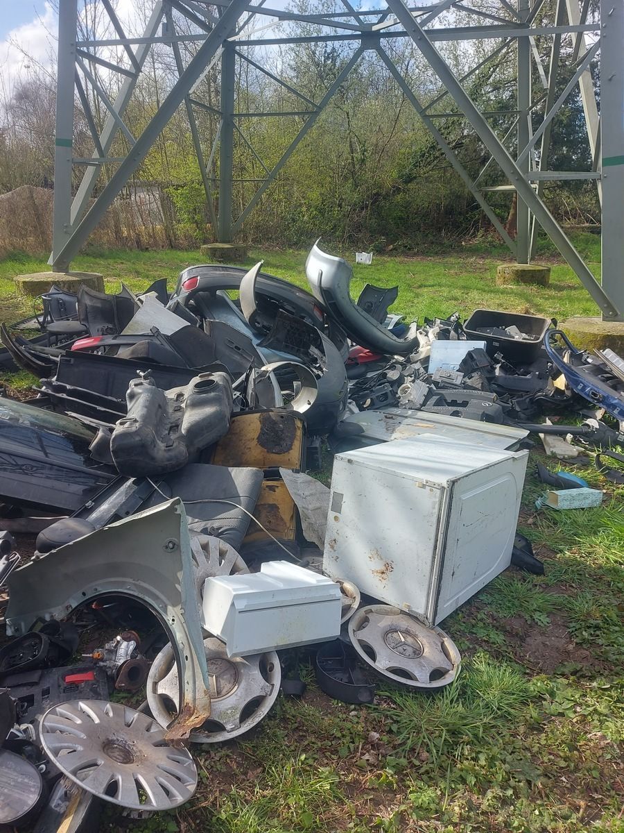 Ein Haufen illegal entsorgter Müll mit Autoteilen liegt in der Natur.