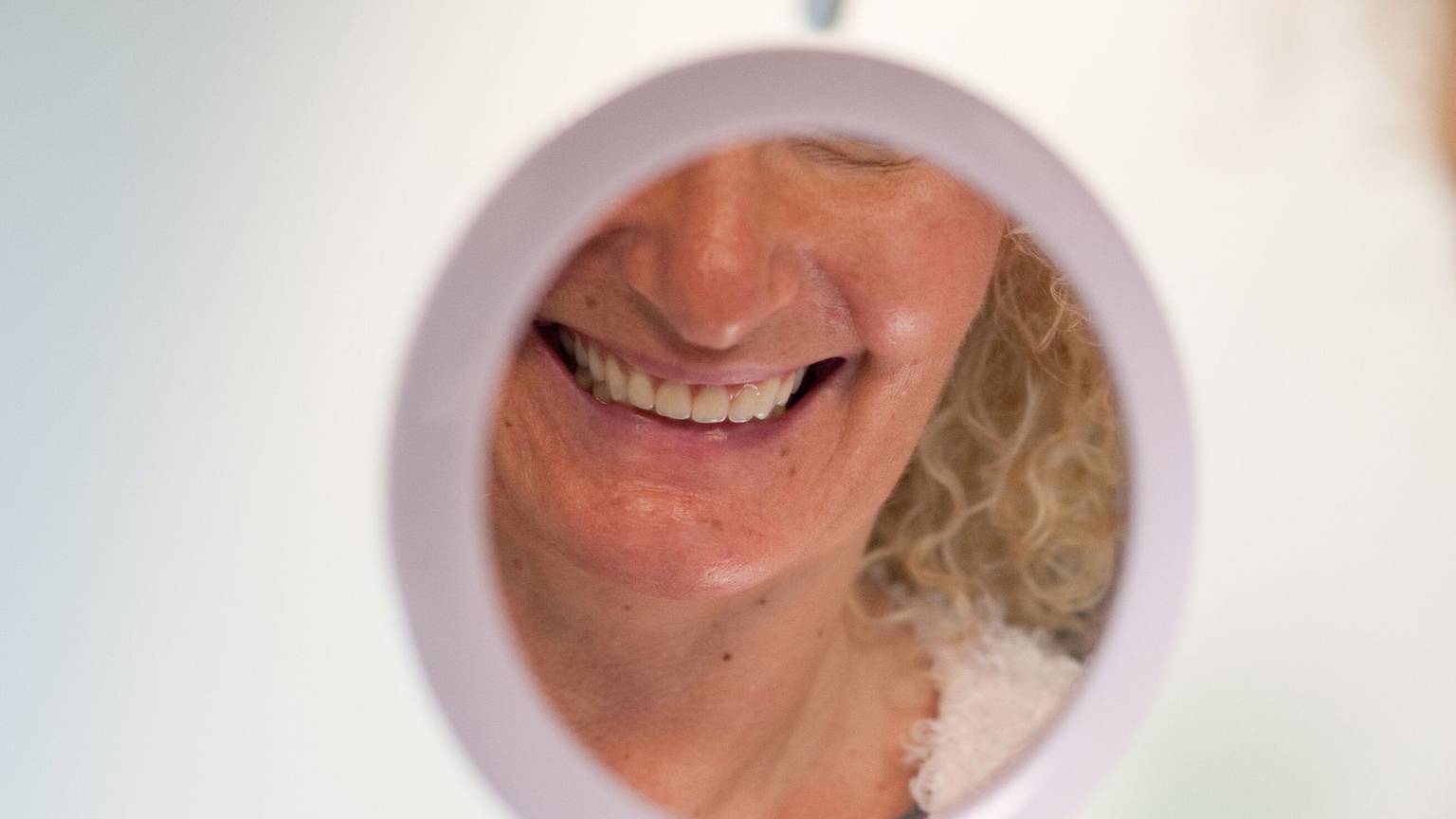 Frau schaut sich ihre Zähne in einem Handspiegel an