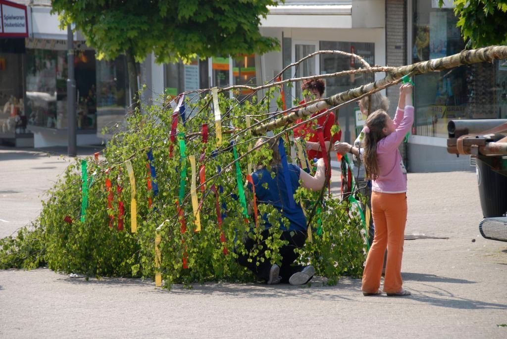 Kinder helfen einen Maibaum zu schmücken.