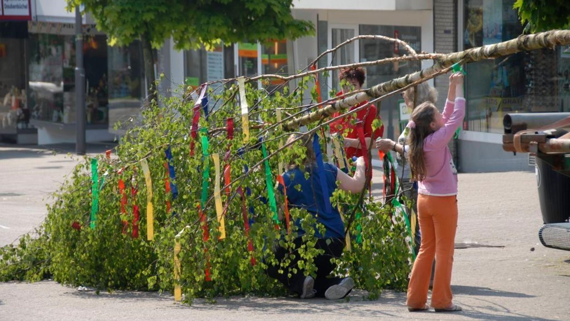 Kinder helfen einen Maibaum zu schmücken.