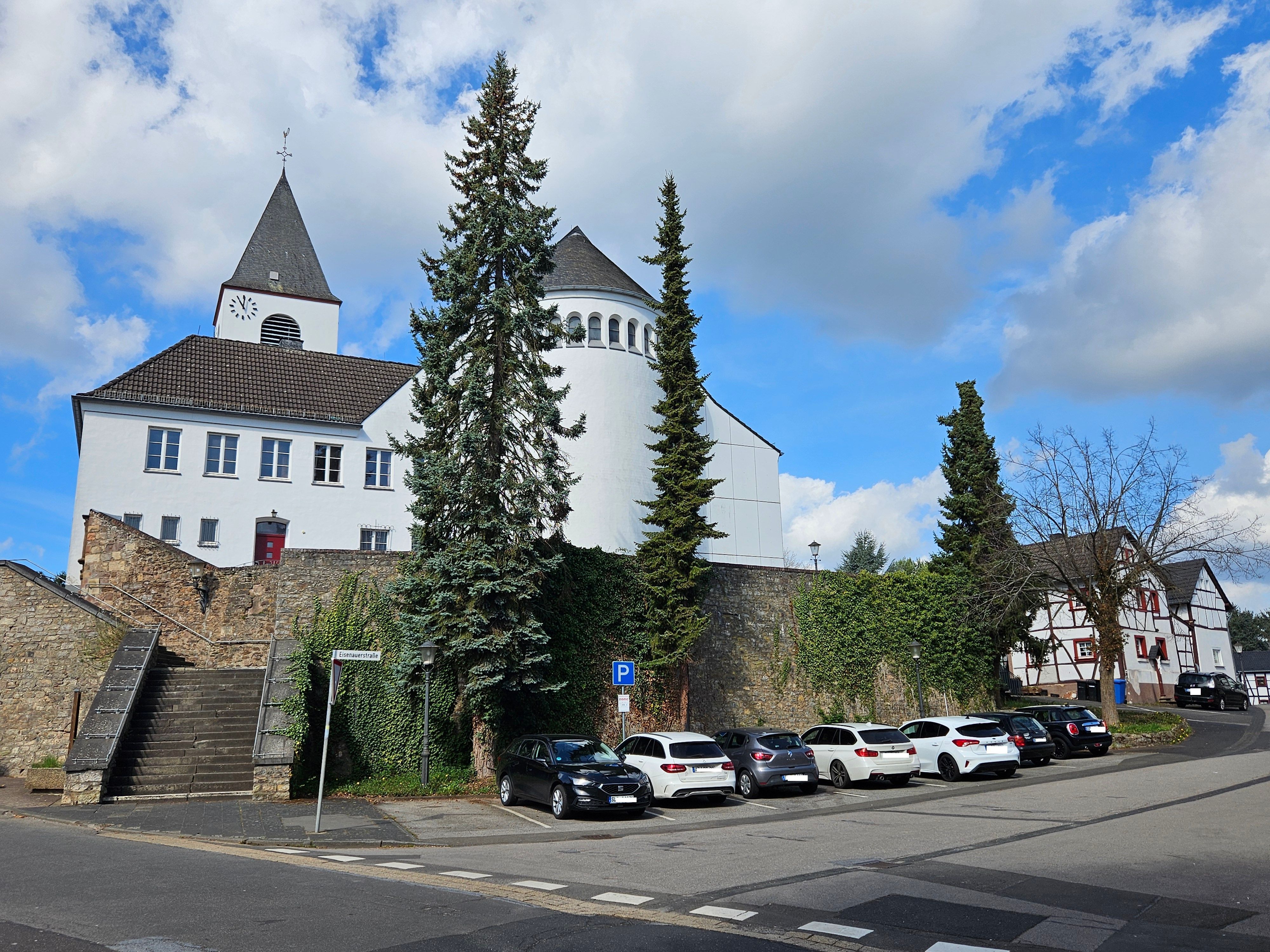 Blick auf die Kirche und die Mauer unterhalb, an der mehrere Autos parken.