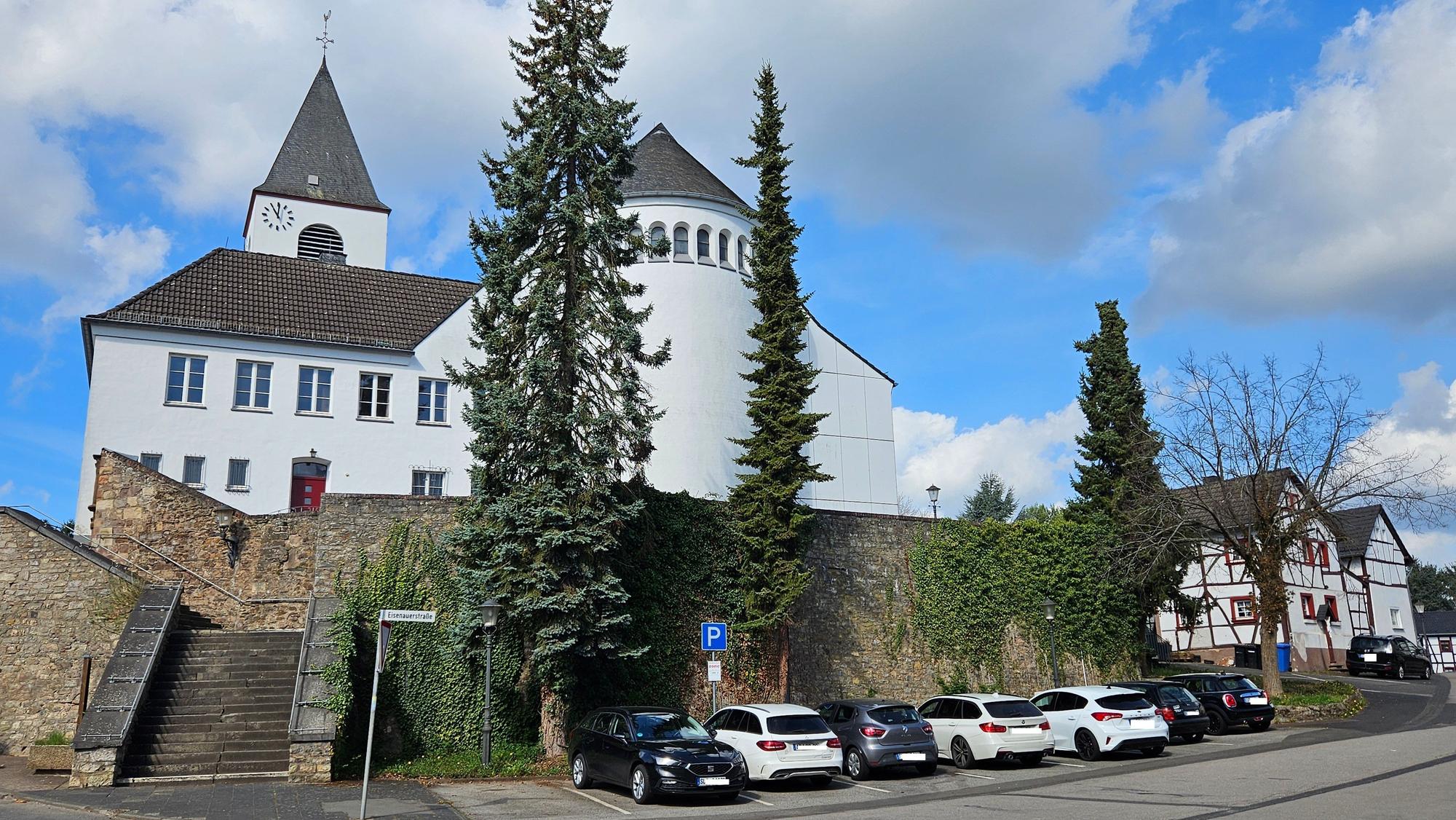 Blick auf die Kirche und die Mauer unterhalb, an der mehrere Autos parken.
