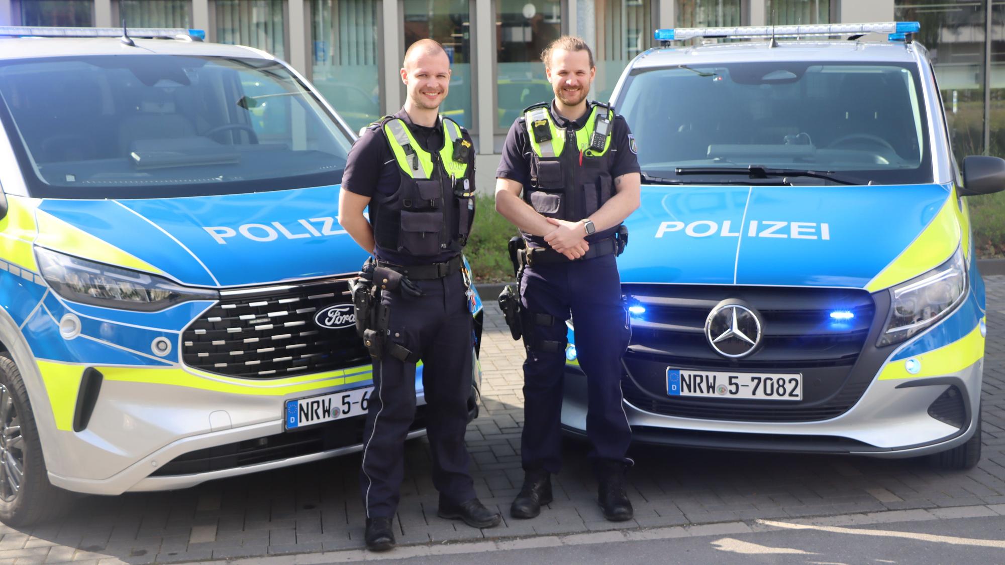 Zwei Polizisten stehen vor zwei Streifenwagen.