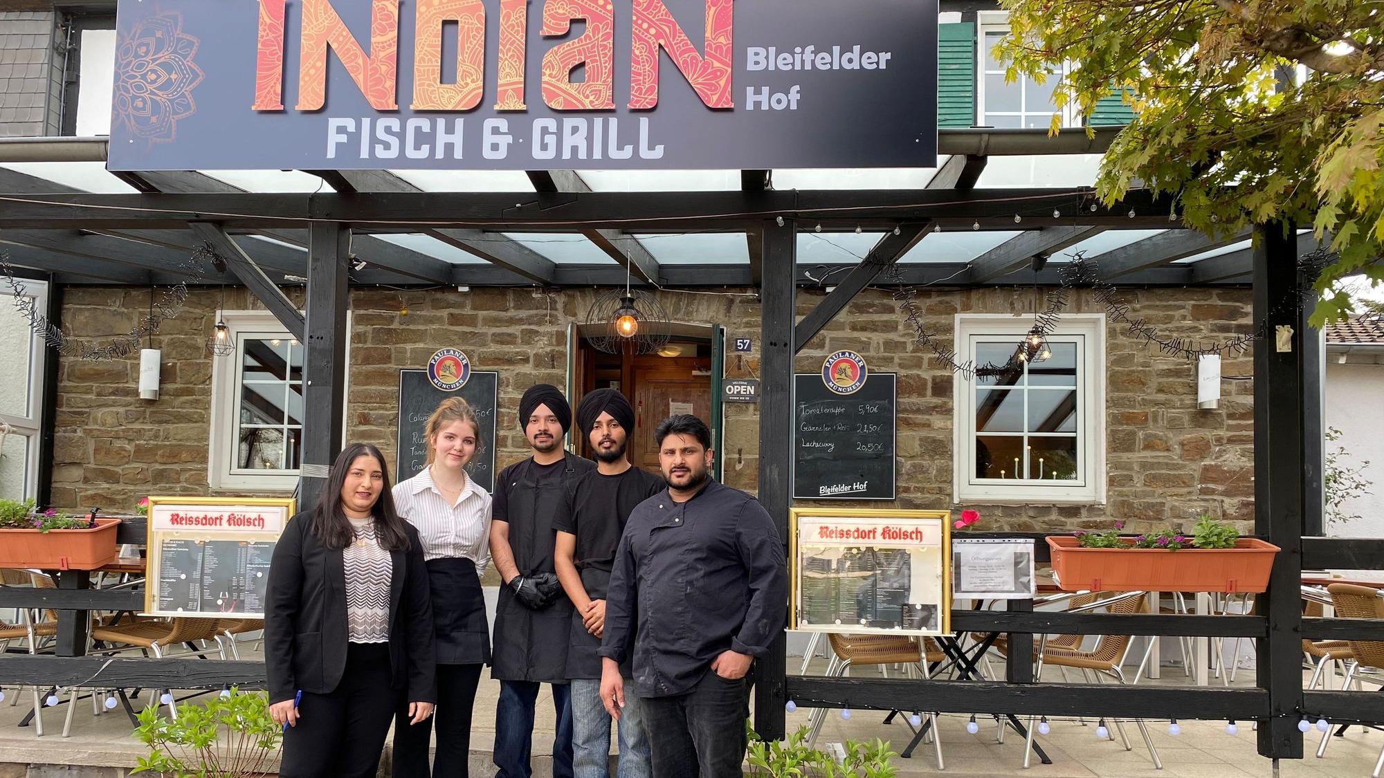 Oben das Schild des Restaurants mit seinem Namen, davor die beiden Inhaber, eine junge Frau aus Bleifeld und zwei junge Männer aus Indien, beide mit schwarzem Turban.