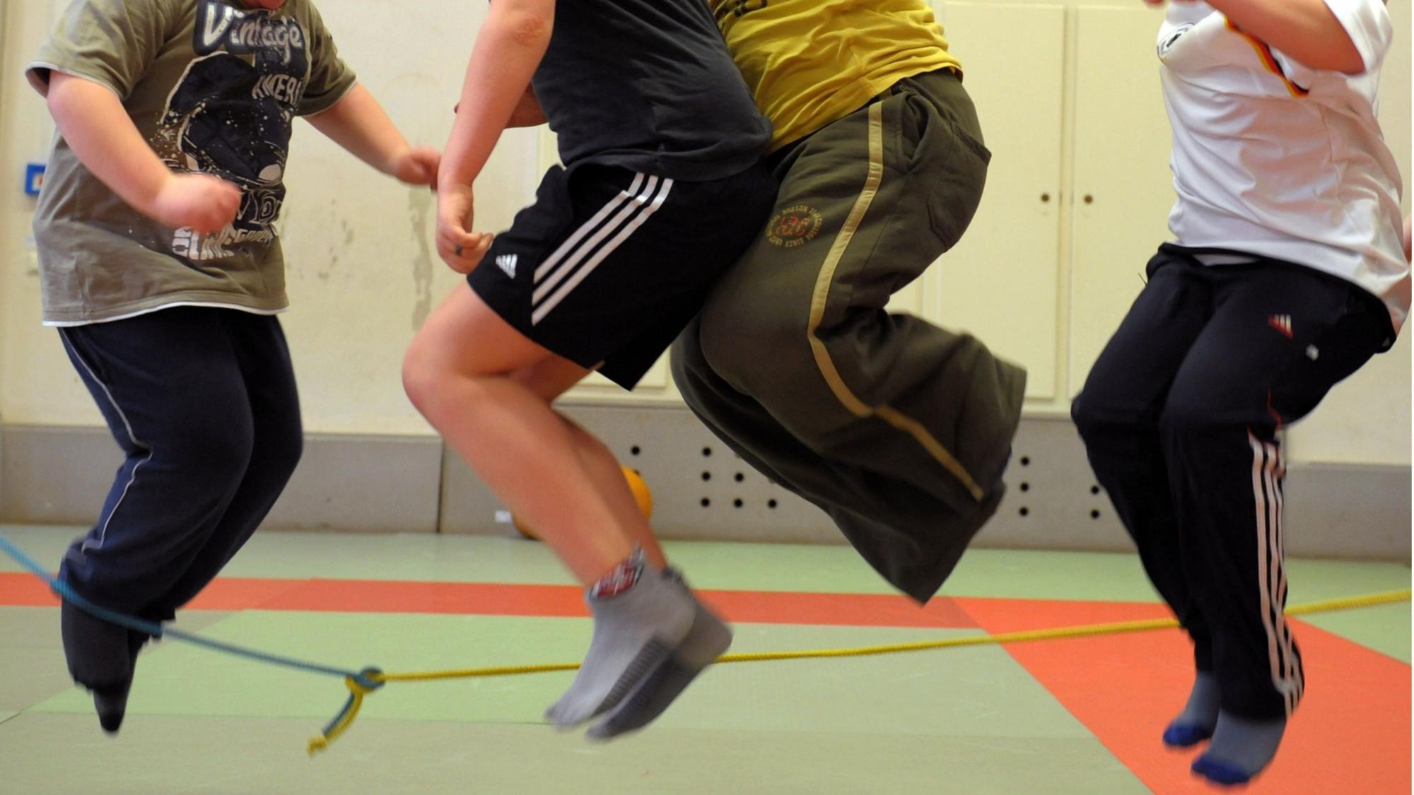 Vier Kinder springen Seil in einer Sporthalle.