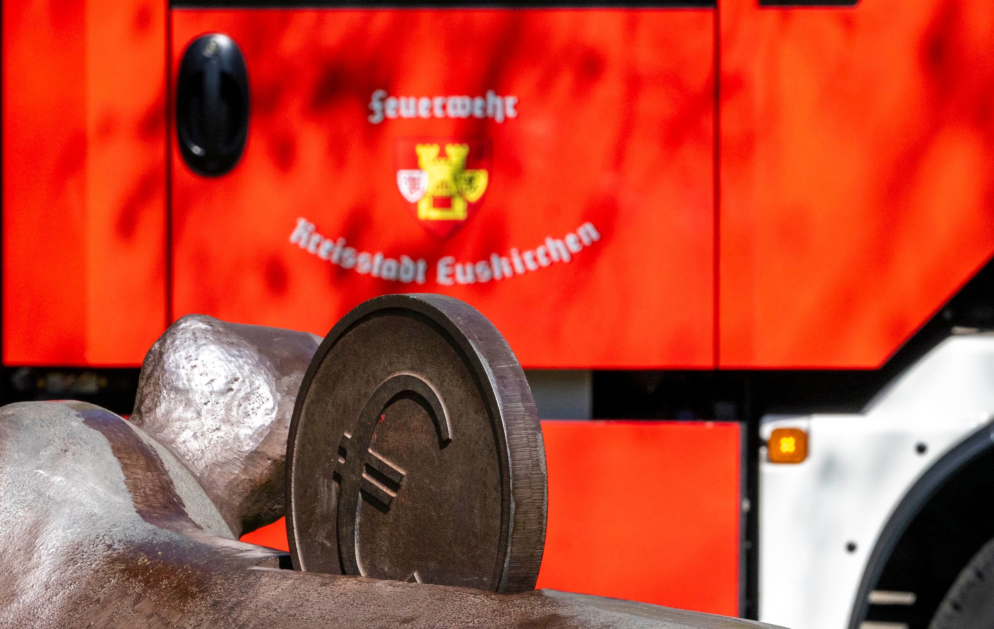 Das Bild zeigt ein Fahrzeug der Euskirchener Feuerwehr. Im Vordergrund ist eine Euro-Münze eines Kunstwerks zu sehen.