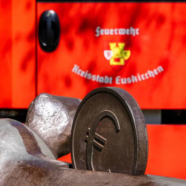 Das Bild zeigt ein Fahrzeug der Euskirchener Feuerwehr. Im Vordergrund ist eine Euro-Münze eines Kunstwerks zu sehen.