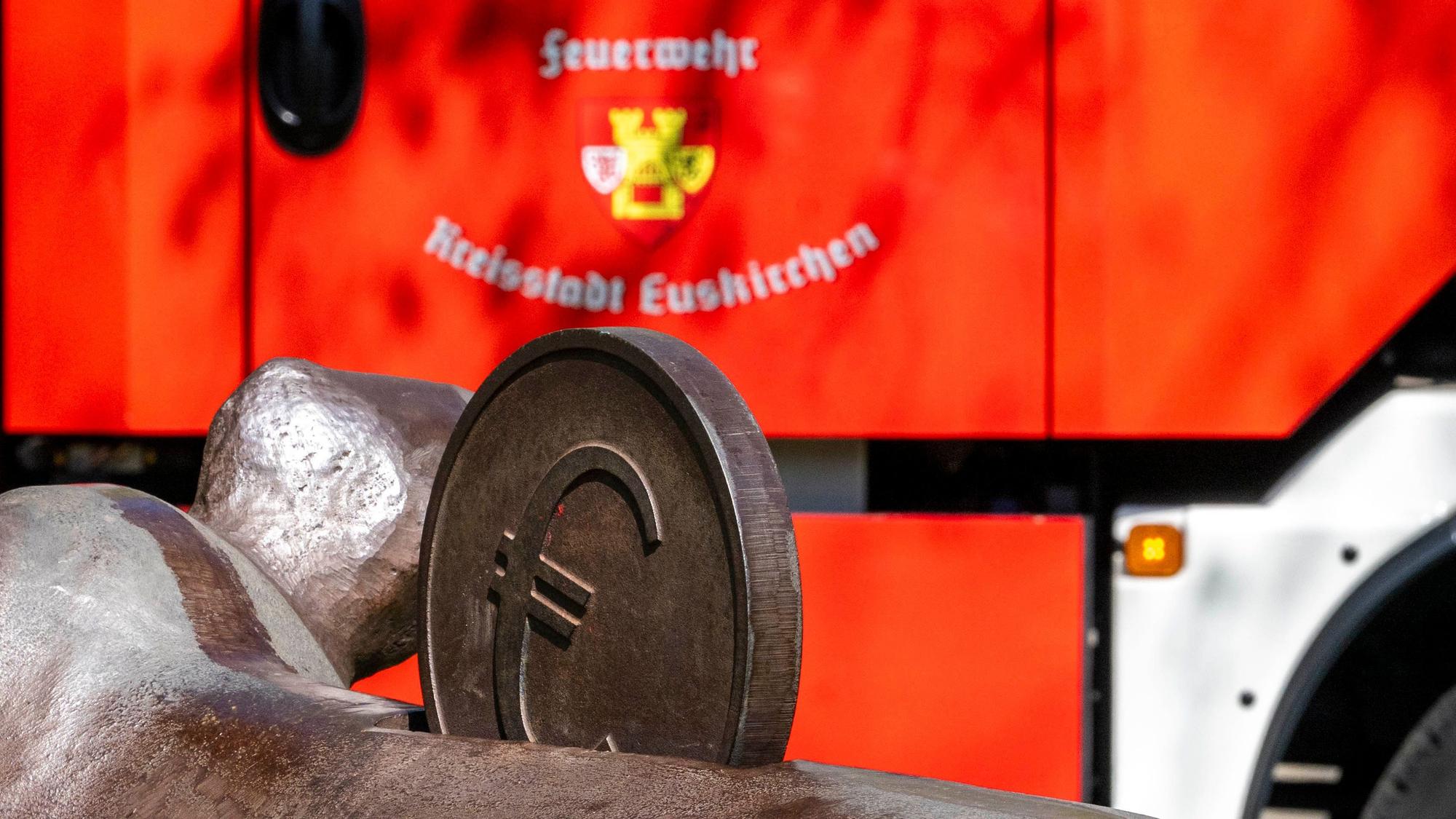 Das Bild zeigt ein Fahrzeug der Euskirchener Feuerwehr. Im Vordergrund ist eine Euro-Münze eines Kunstwerks zu sehen.
