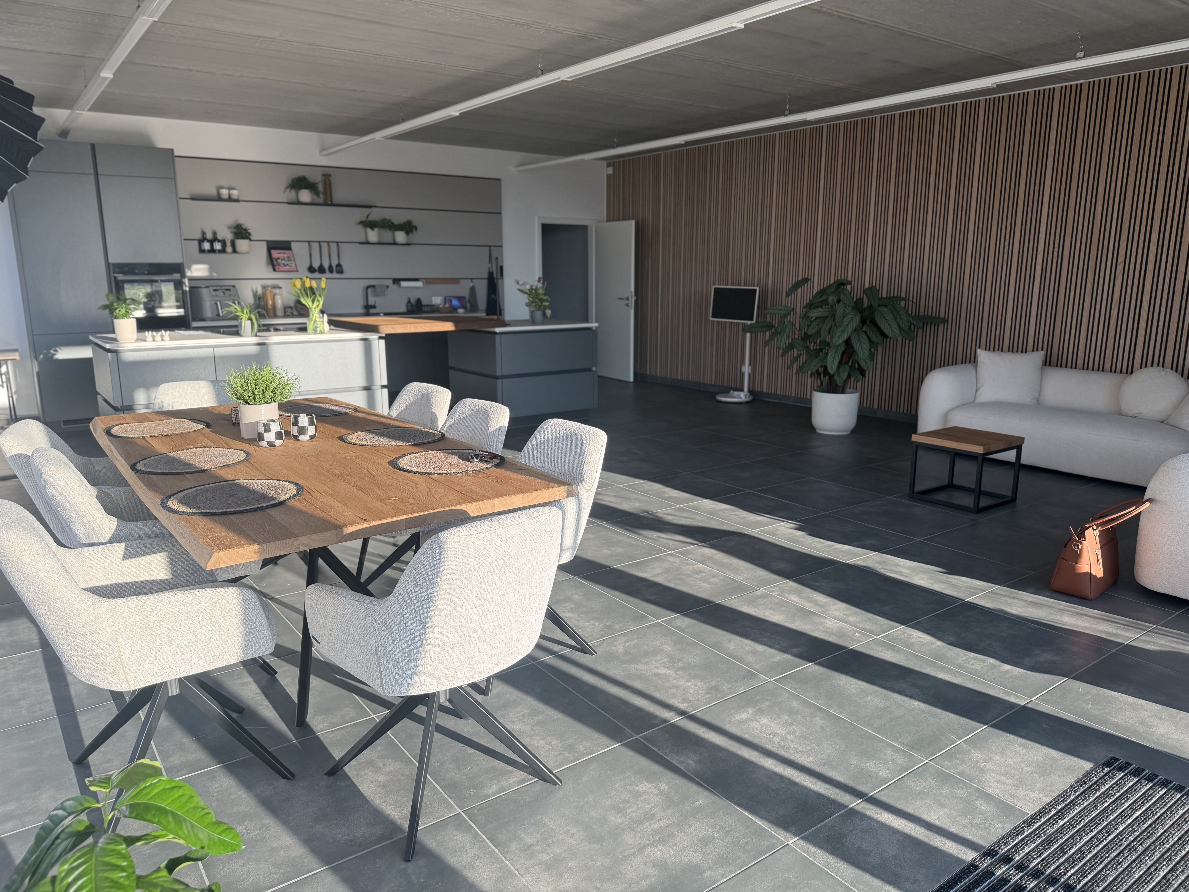 Das Bild zeigt ein Kochstudio mit Küche, Kücheninsel, großem Esstisch und Couch.