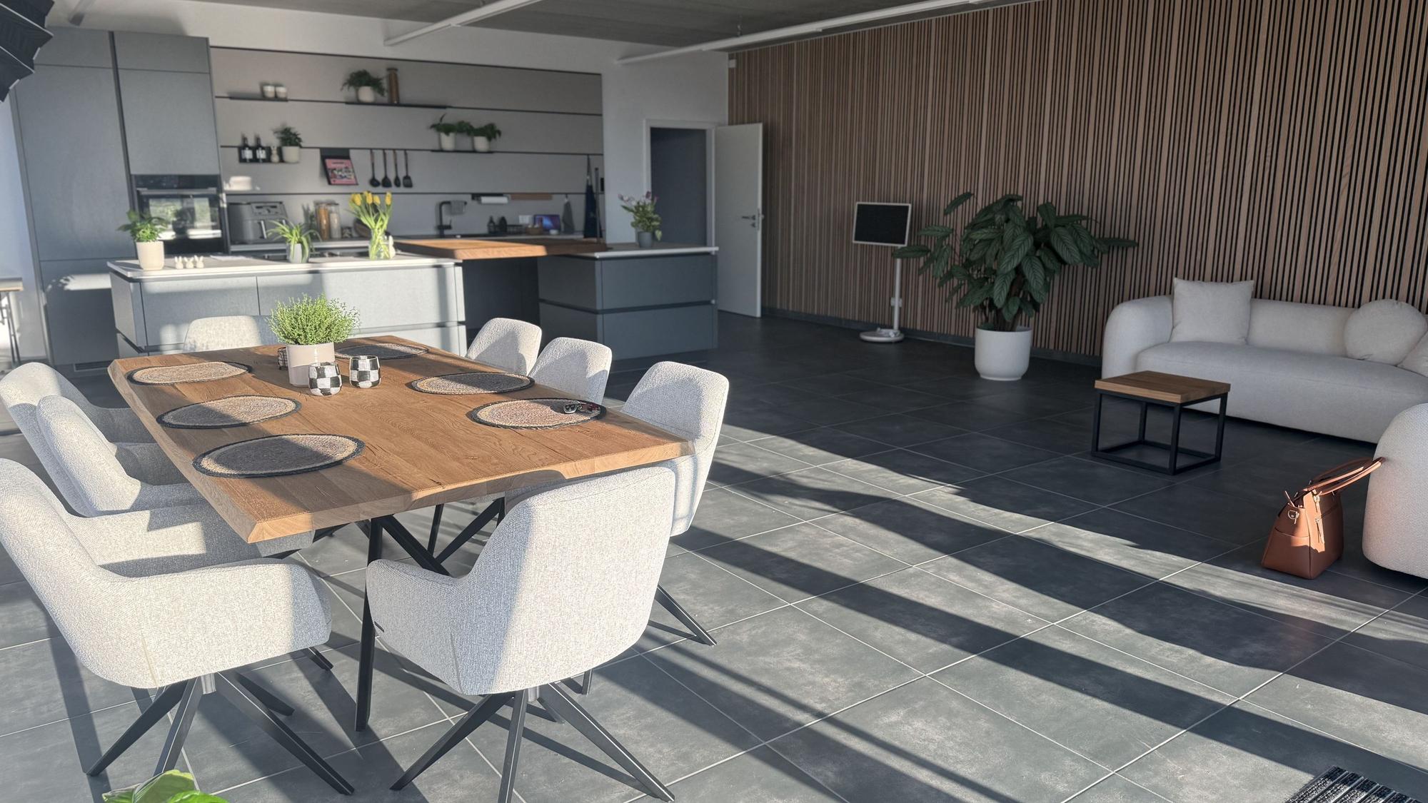 Das Bild zeigt ein Kochstudio mit Küche, Kücheninsel, großem Esstisch und Couch.
